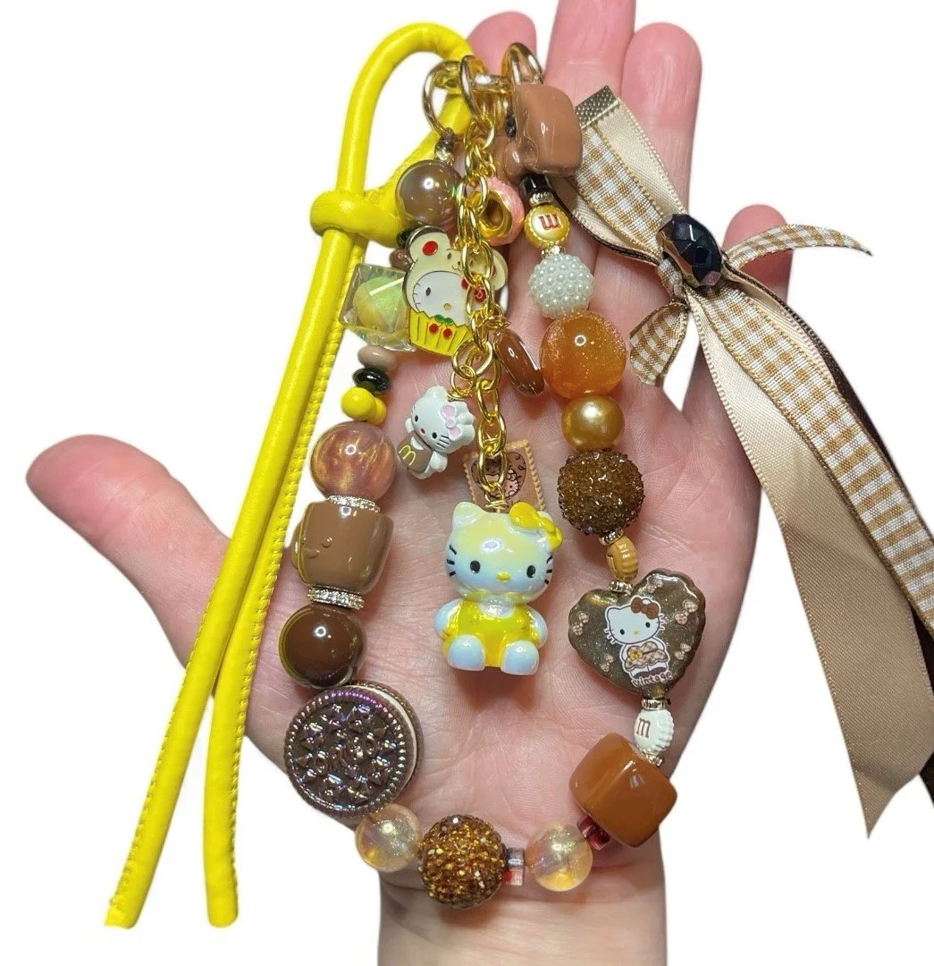Hand holding colorful Hello Kitty-themed keychains with beads and a ribbon.