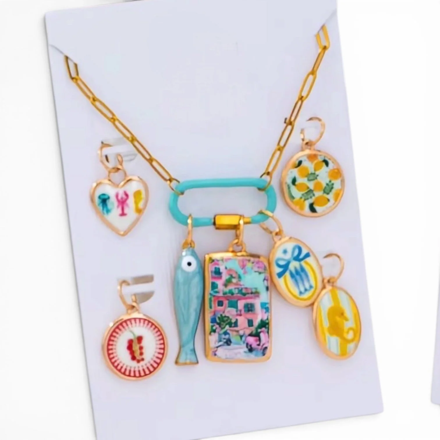 Colorful fashion jewelry with charms on a white background, including a fish, a gift box, a lemon, a red circle with a pattern, and other decorative pendants.