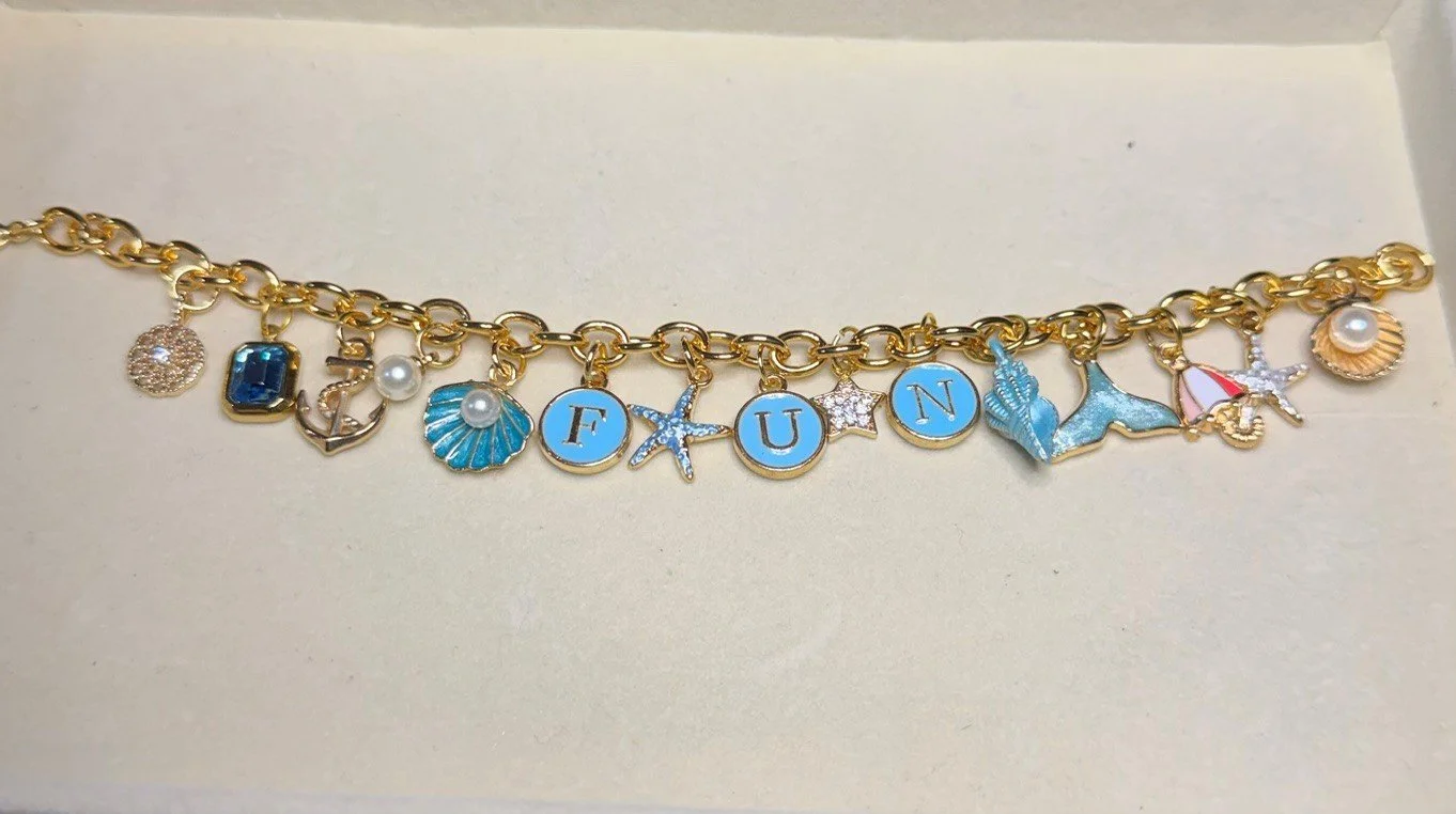 Gold charm bracelet with ocean-themed charms and the word "FUN" spelled out with blue and white beads.