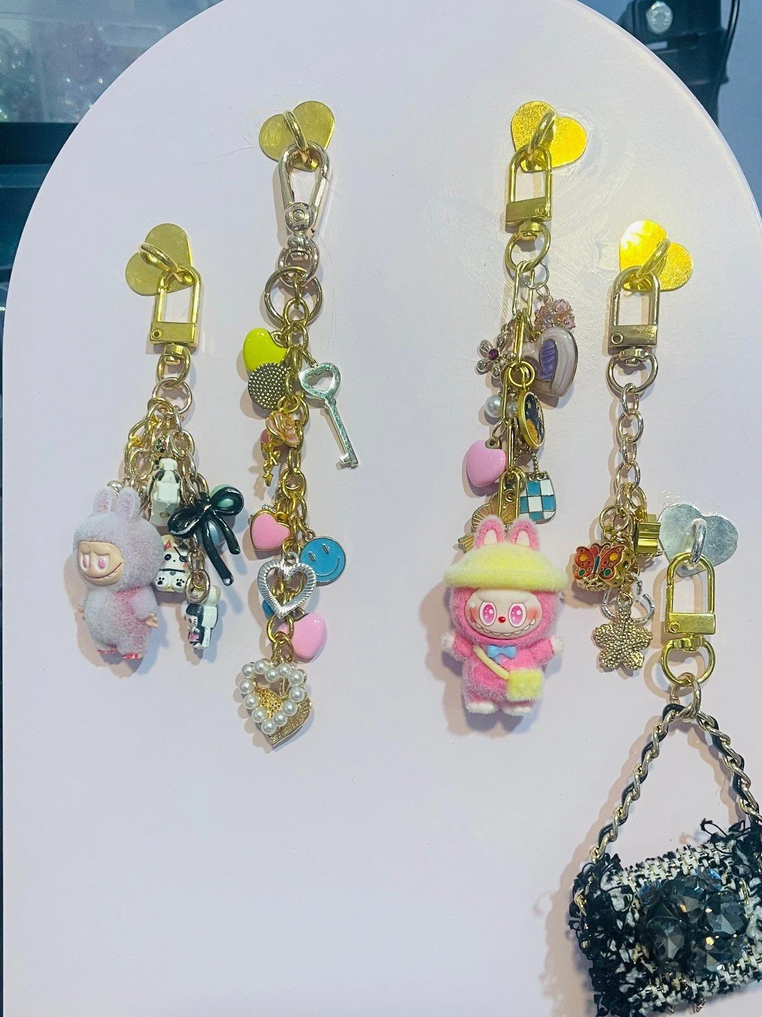 Four colorful keychains with plush characters, charms, and beads hanging from yellow heart-shaped clips.