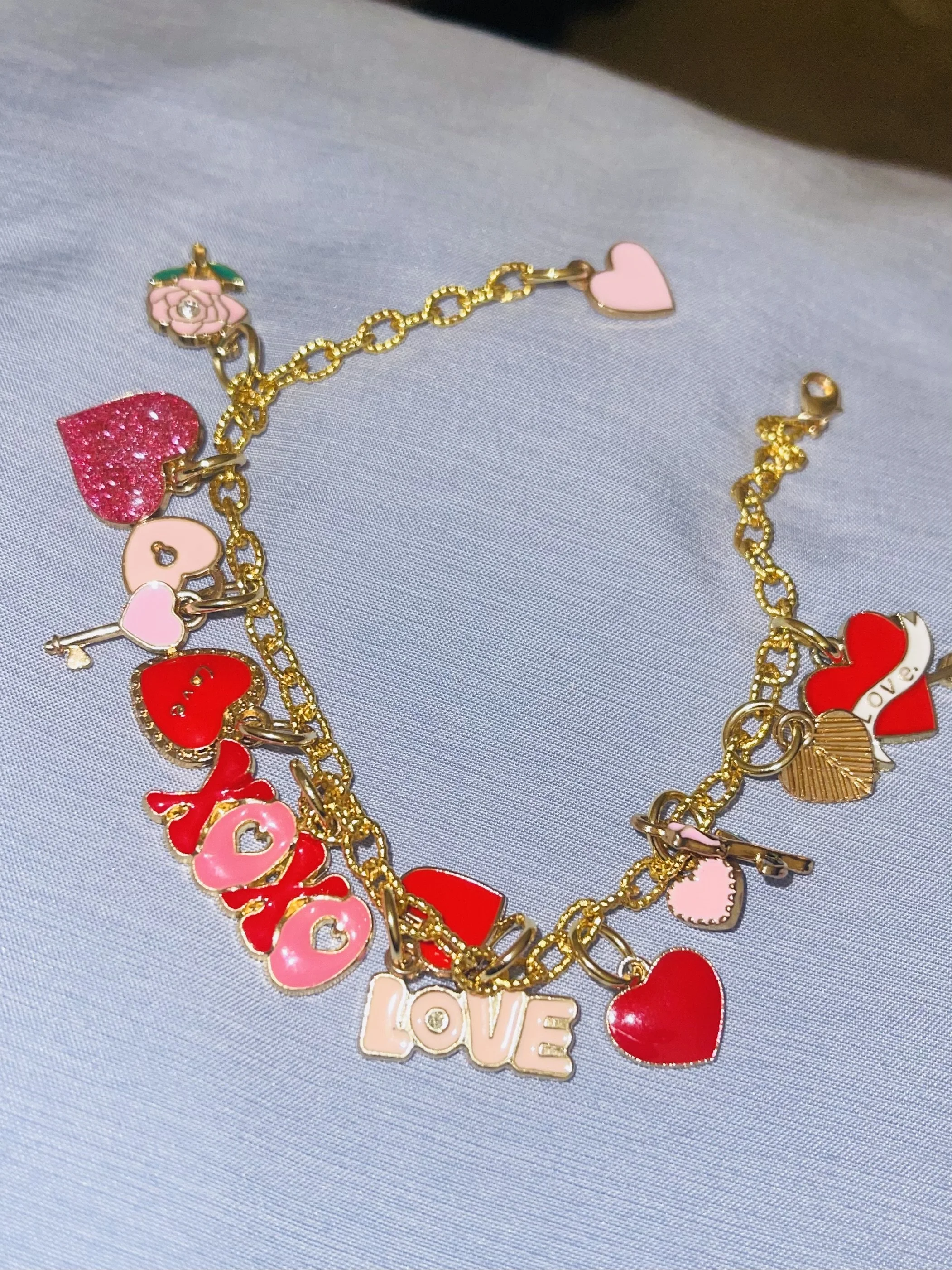Gold chain necklace with various pink, red, and gold love-themed charms, including hearts, the word 'LOVE,' and other decorative pendants.