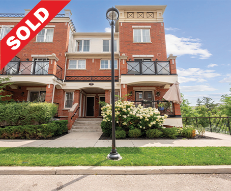 Multi-story brick residential building with balconies and a sold sign in the front yard, plus a sidewalk and greenery.