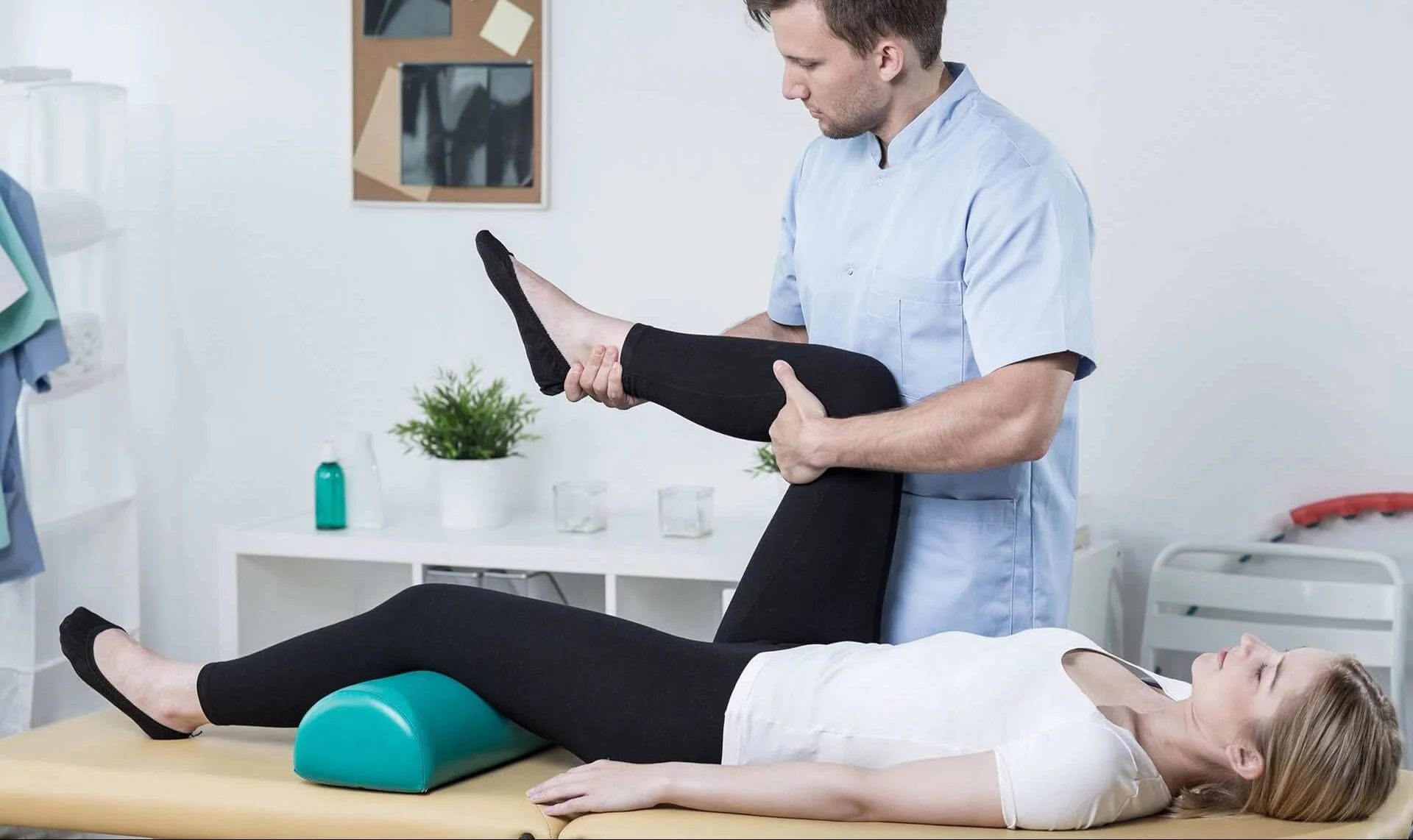 A physical therapist lifts a woman's leg during a therapy session in a clinic.