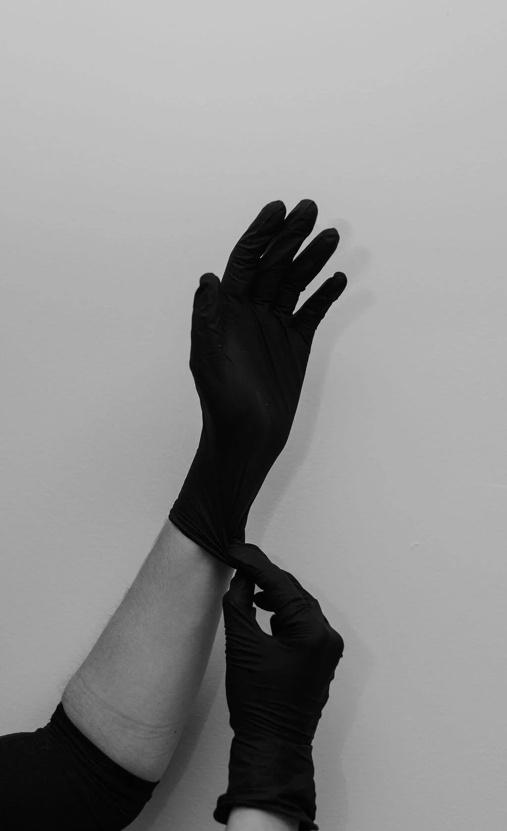 A person's arm wearing a black glove, with the other hand adjusting the glove on the wrist against a plain white background.