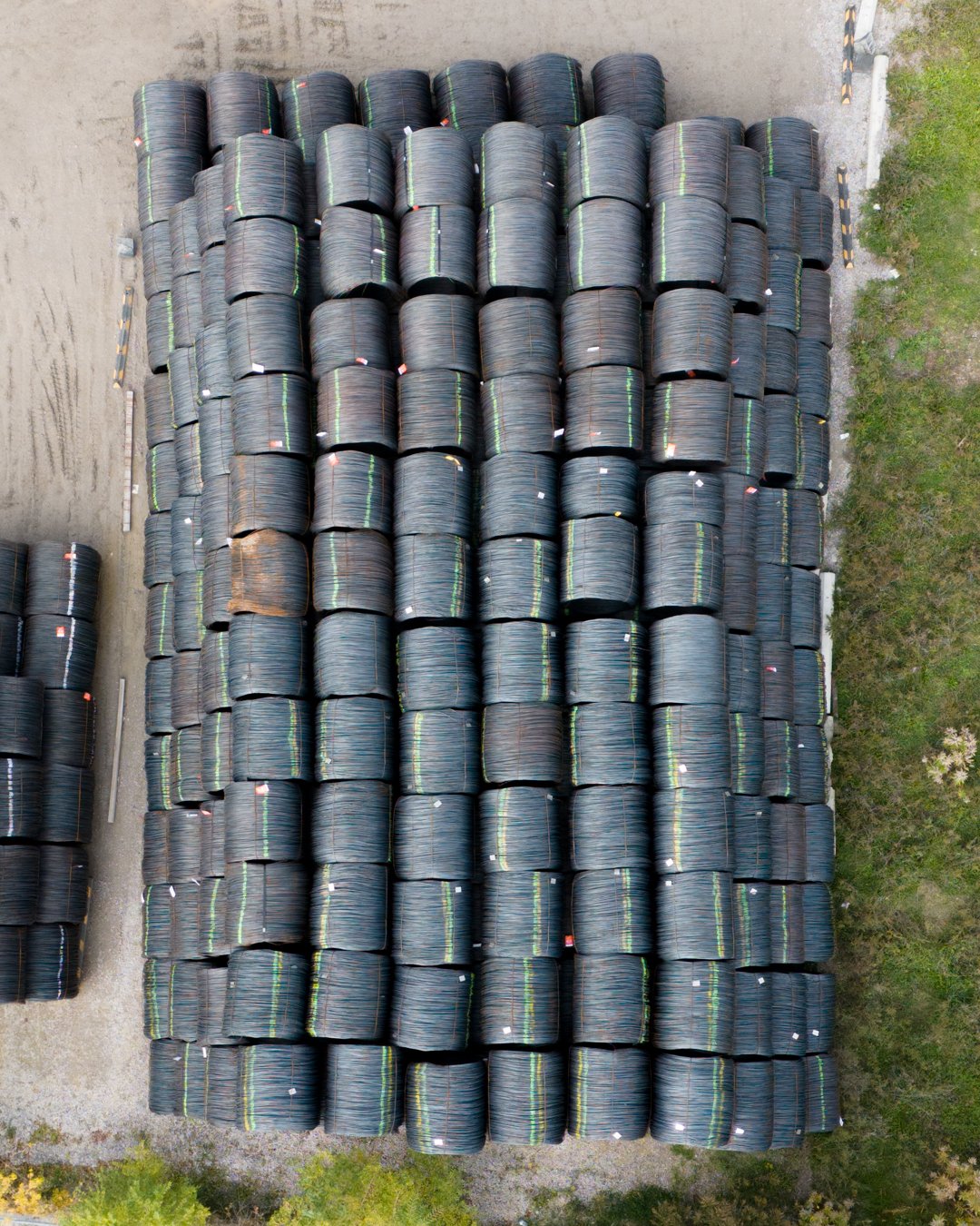 Aerial view of large stacks of rolled black wire spools in an outdoor storage yard.