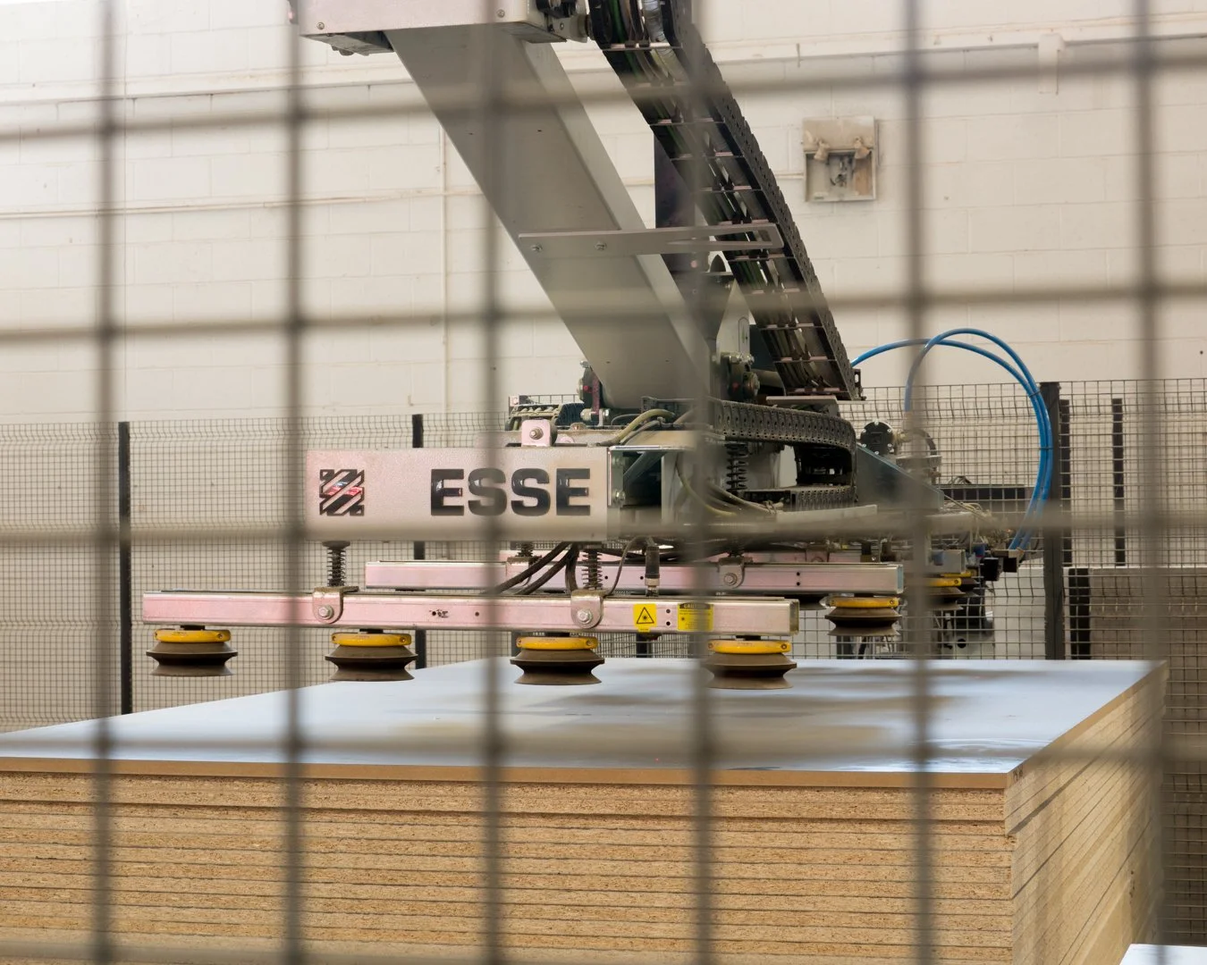 A robotic machine labeled 'ESSE' is moving large sheets of plywood in a manufacturing or industrial setting.