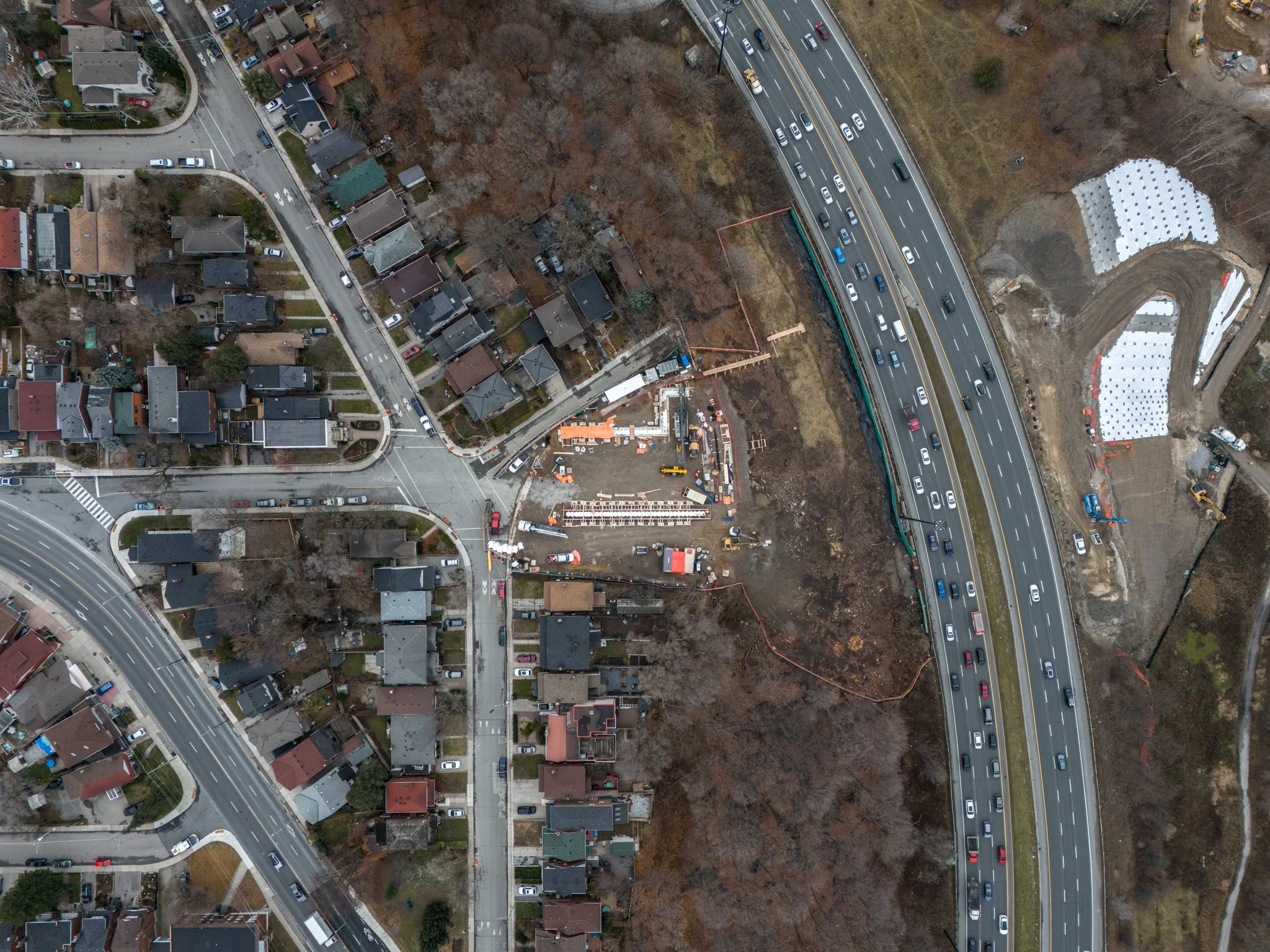 An aerial view of a construction zone in a residential neighborhood with a highway, houses, trees, and suburban houses.