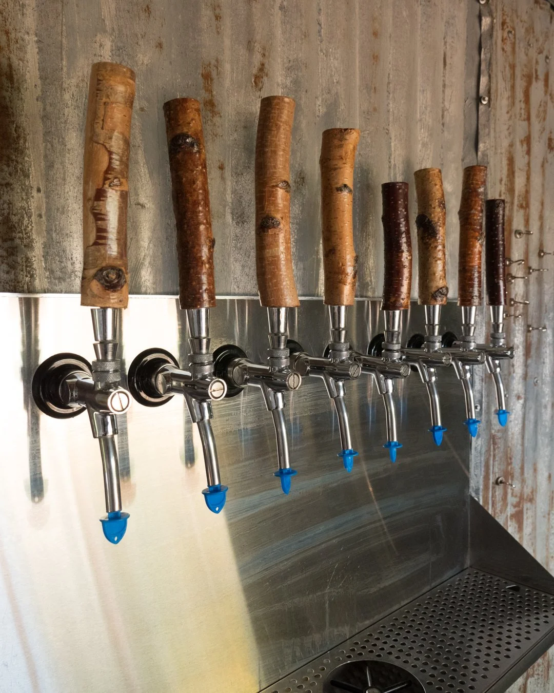 Multiple beer taps with wooden handles mounted on a metallic wall.