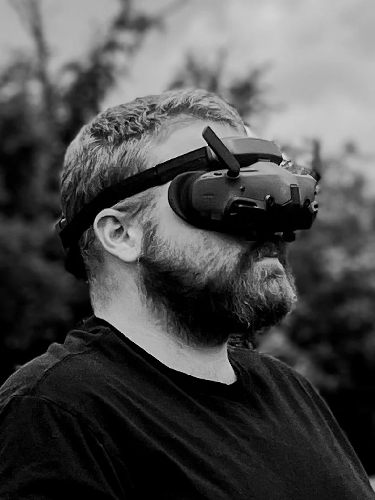 A man with a beard and short hair wearing an fpv drone headset outdoors in black and white.