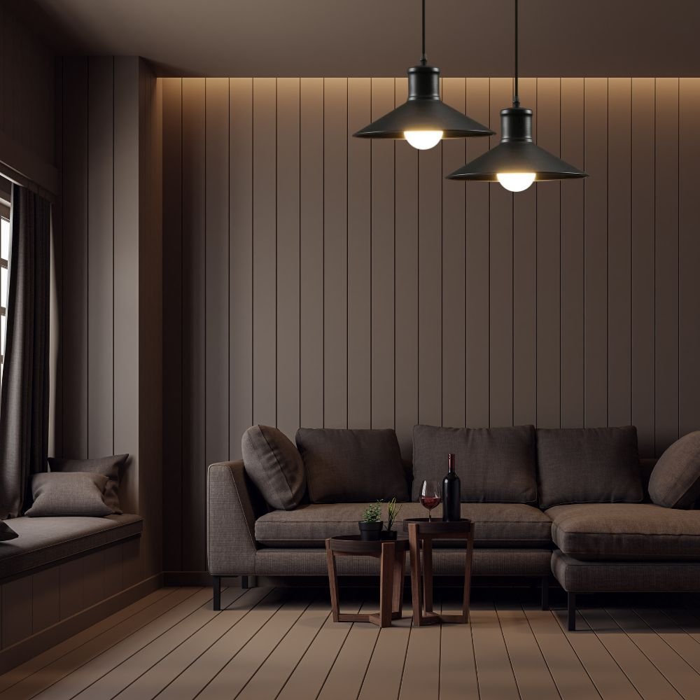 Living room with dark wood paneled wall, beige sofa with cushions, two small nesting tables with a wine bottle, glass of wine, and small plant, pendant lights hanging from ceiling, window with dark curtains.