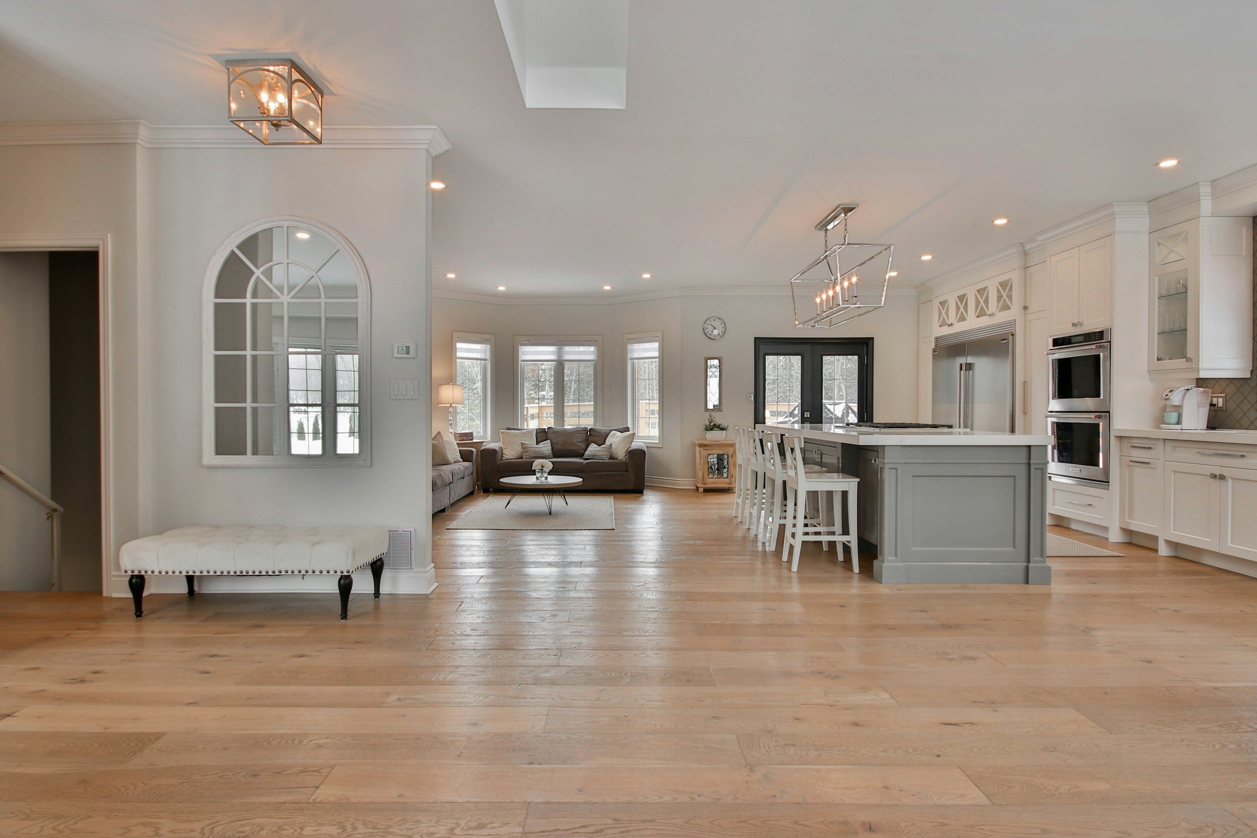 Spacious open-concept kitchen and living area with vinyl floors, white cabinetry, and large windows.