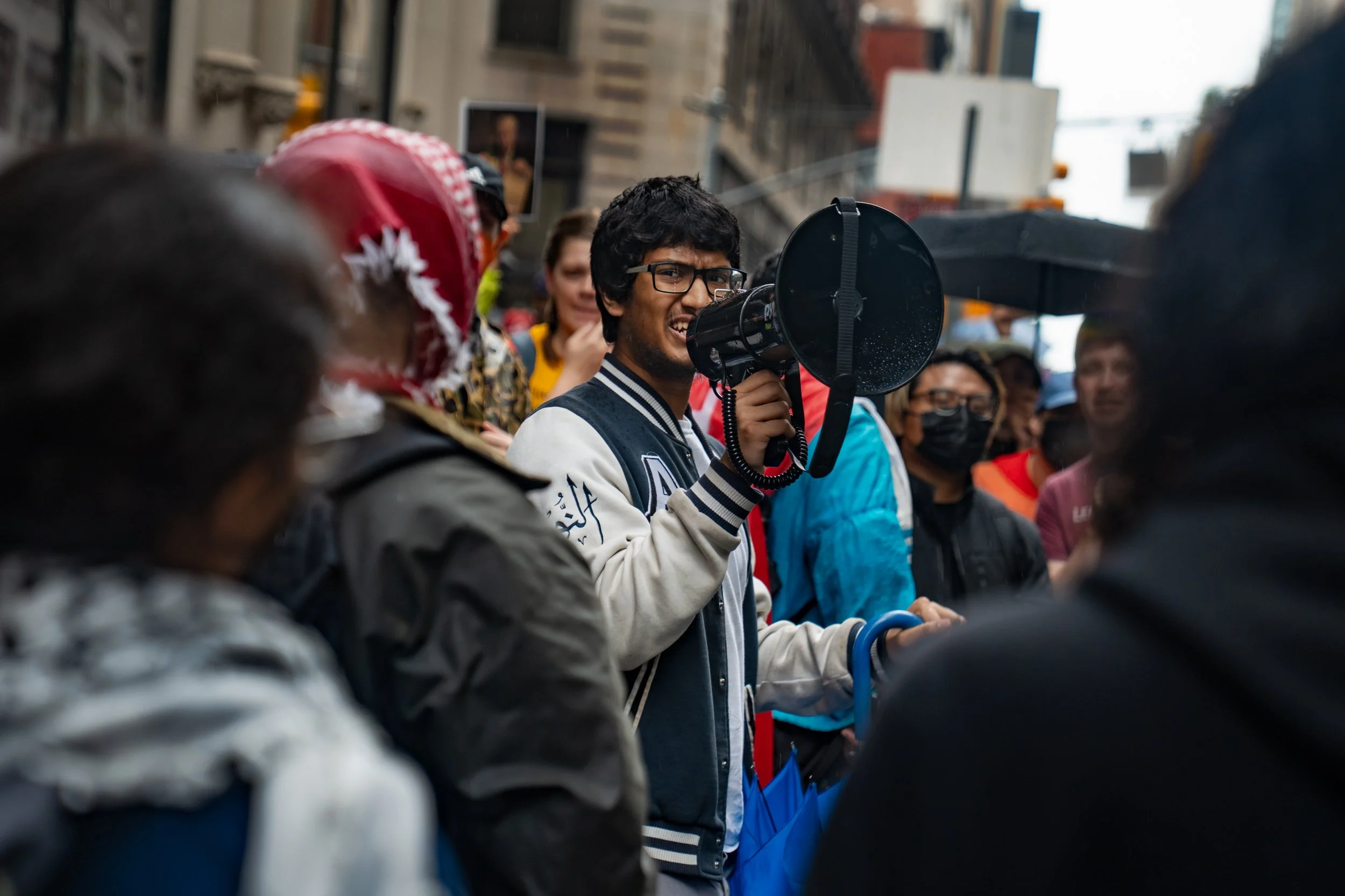 Person speaking into a megaphone at a crowded street protest.
