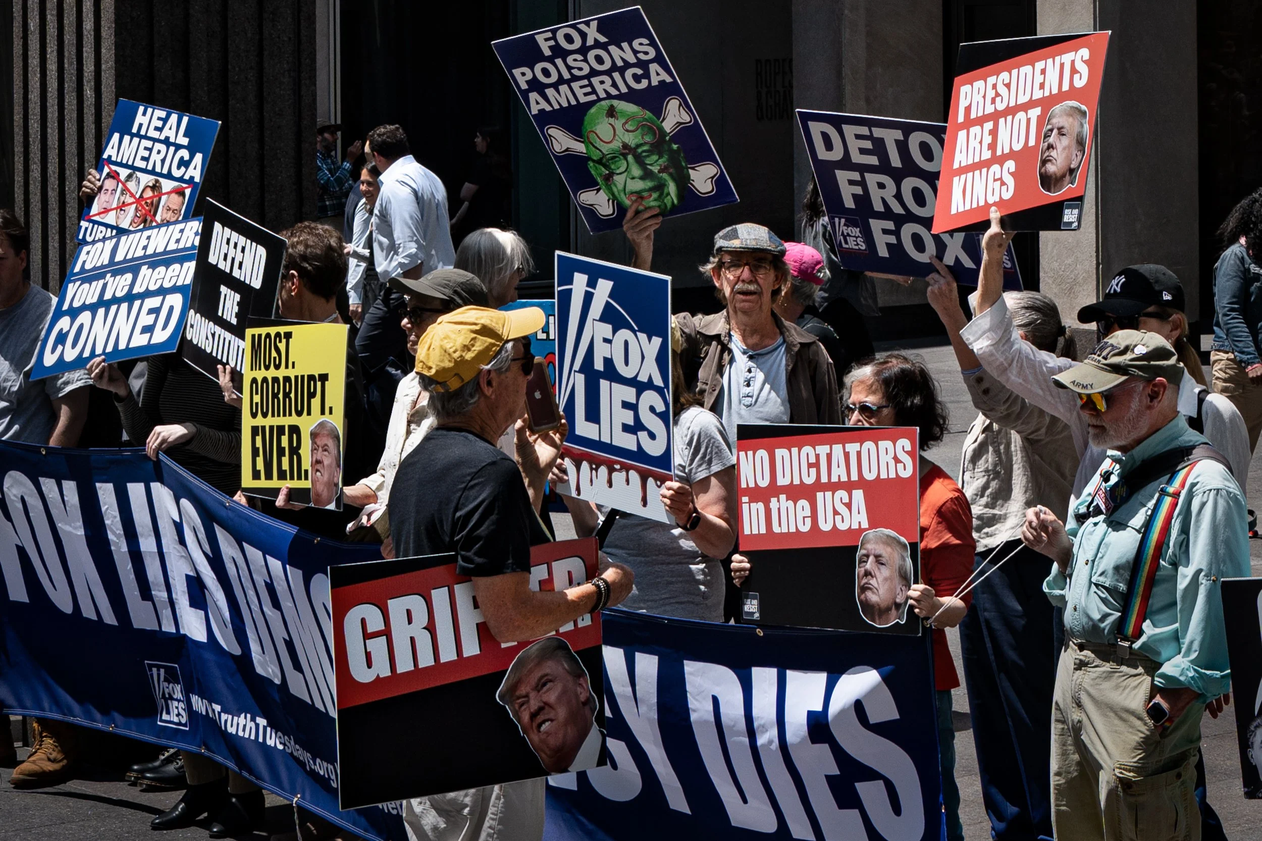 A group of protesters holding signs criticizing Fox News and Donald Trump during a demonstration.