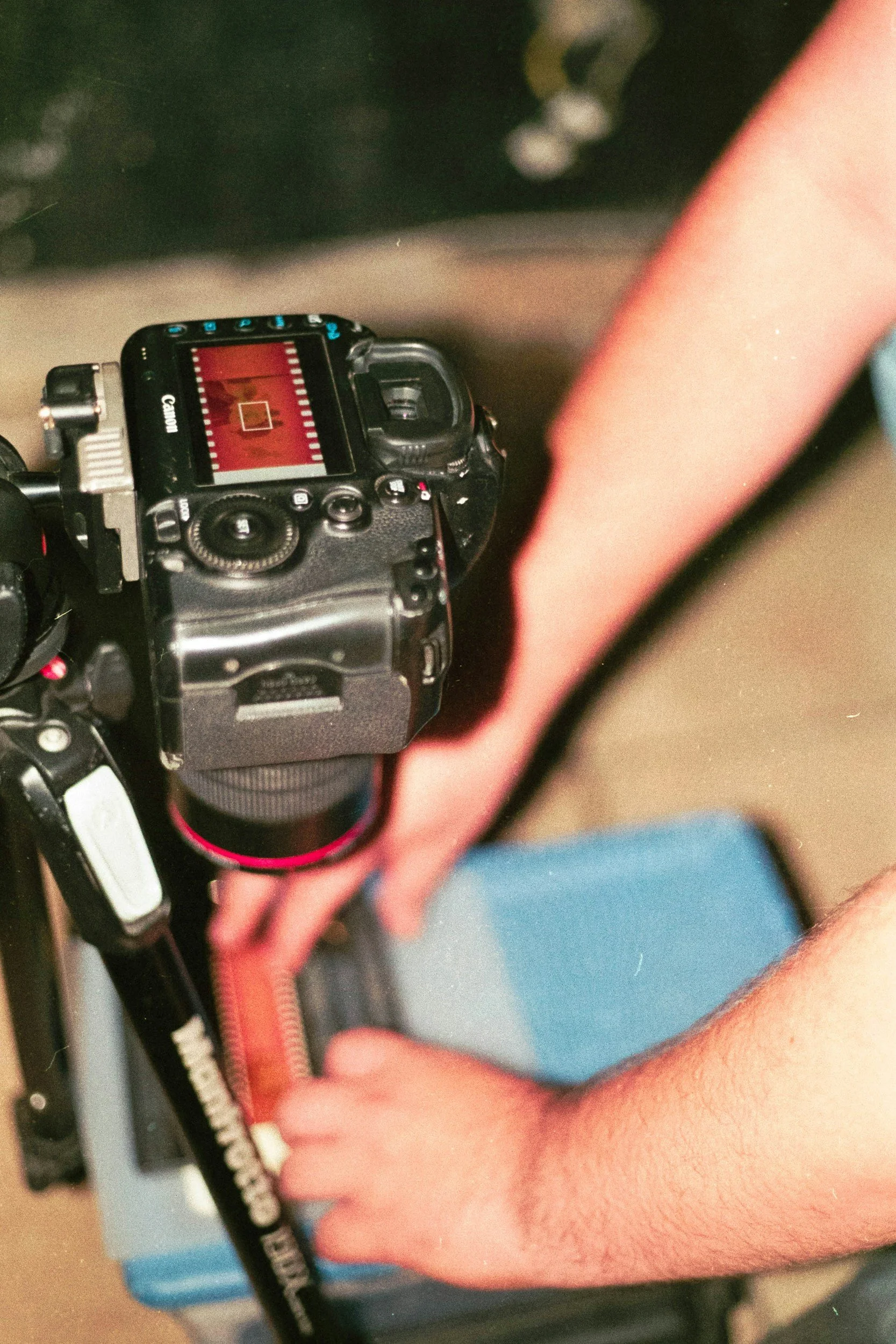A person's hand holding a Canon camera positioned above a blue and black box.