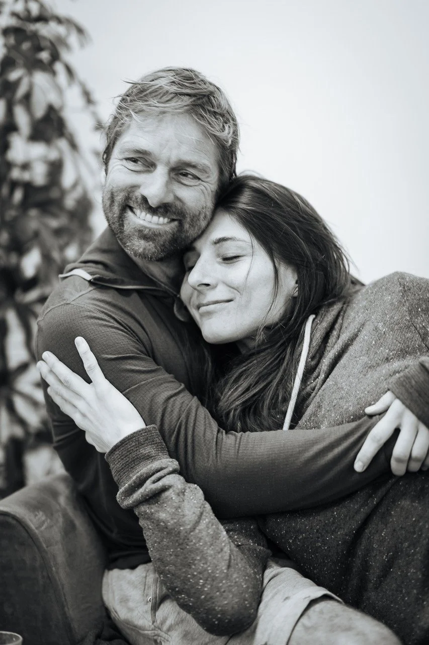 A black and white photo of a couple hugging and smiling, with the woman’s eyes closed and the man looking off to the side.