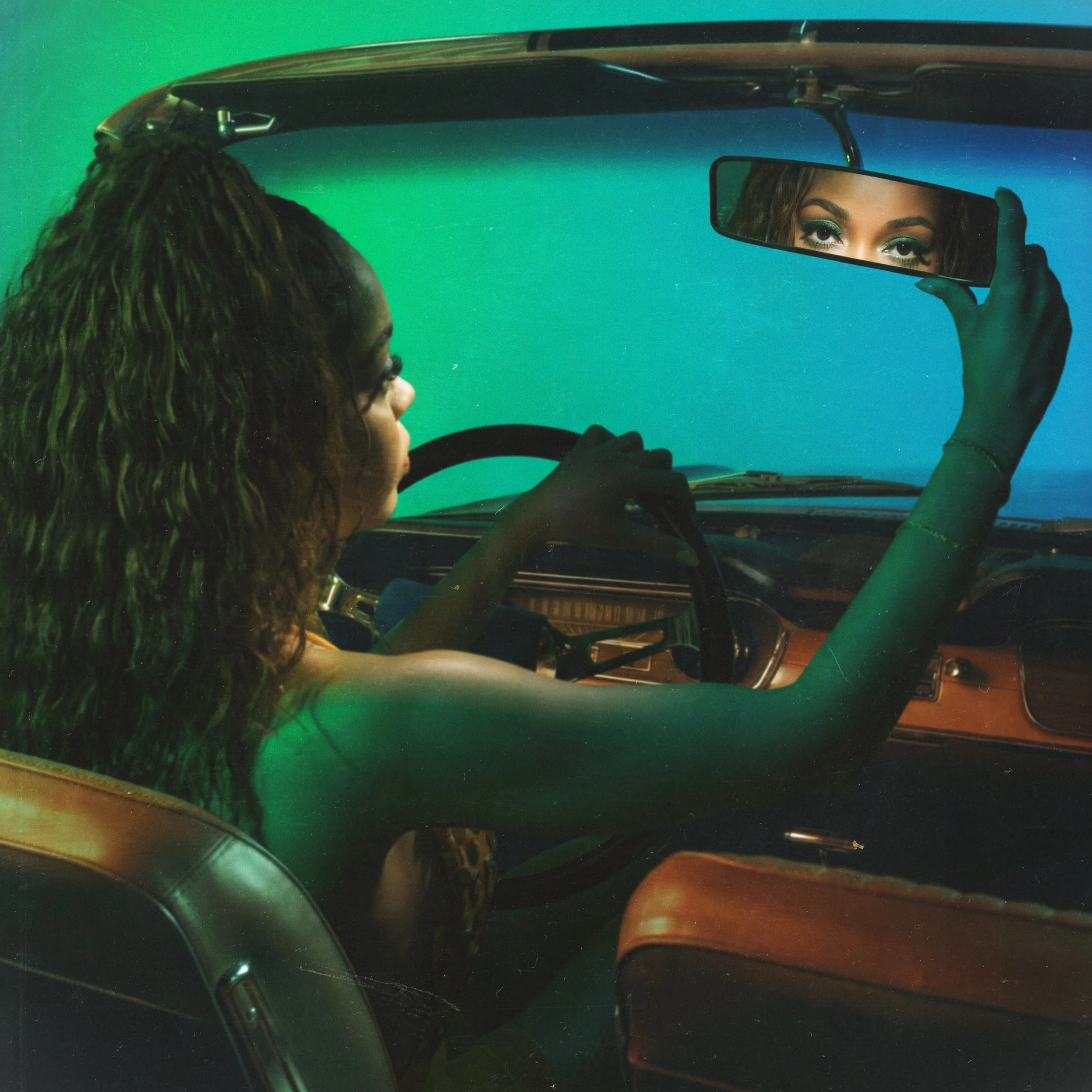 A woman with curly hair in a vintage car, adjusting the rearview mirror to look at her reflection, with a green and blue gradient background.