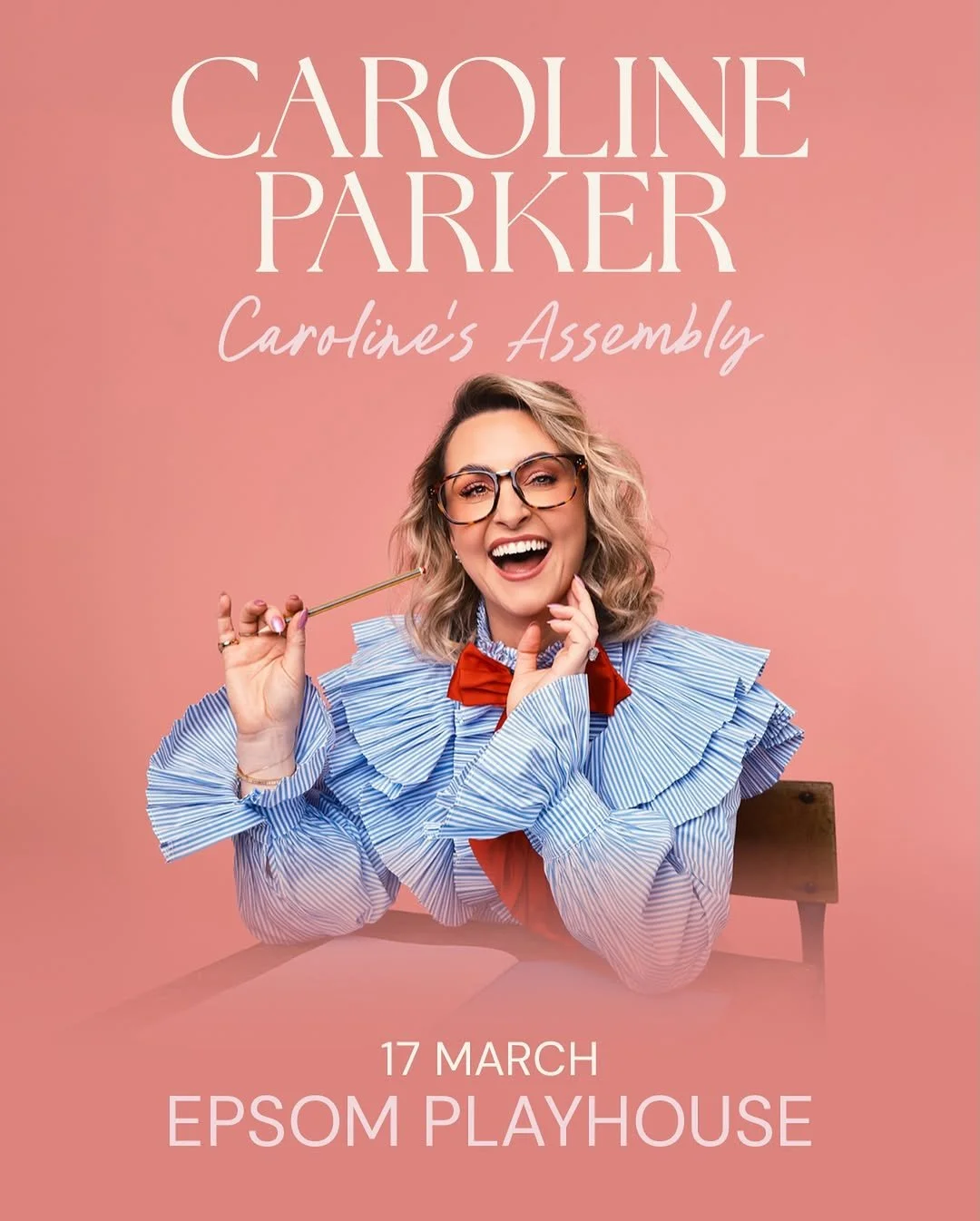 Promotional poster for Caroline Parker's event 'Caroline's Assembly' at Epsom Playhouse on March 17. The poster features a woman with blonde curly hair, glasses, and a striped blue and white blouse with ruffles, smiling and holding a golden pen.