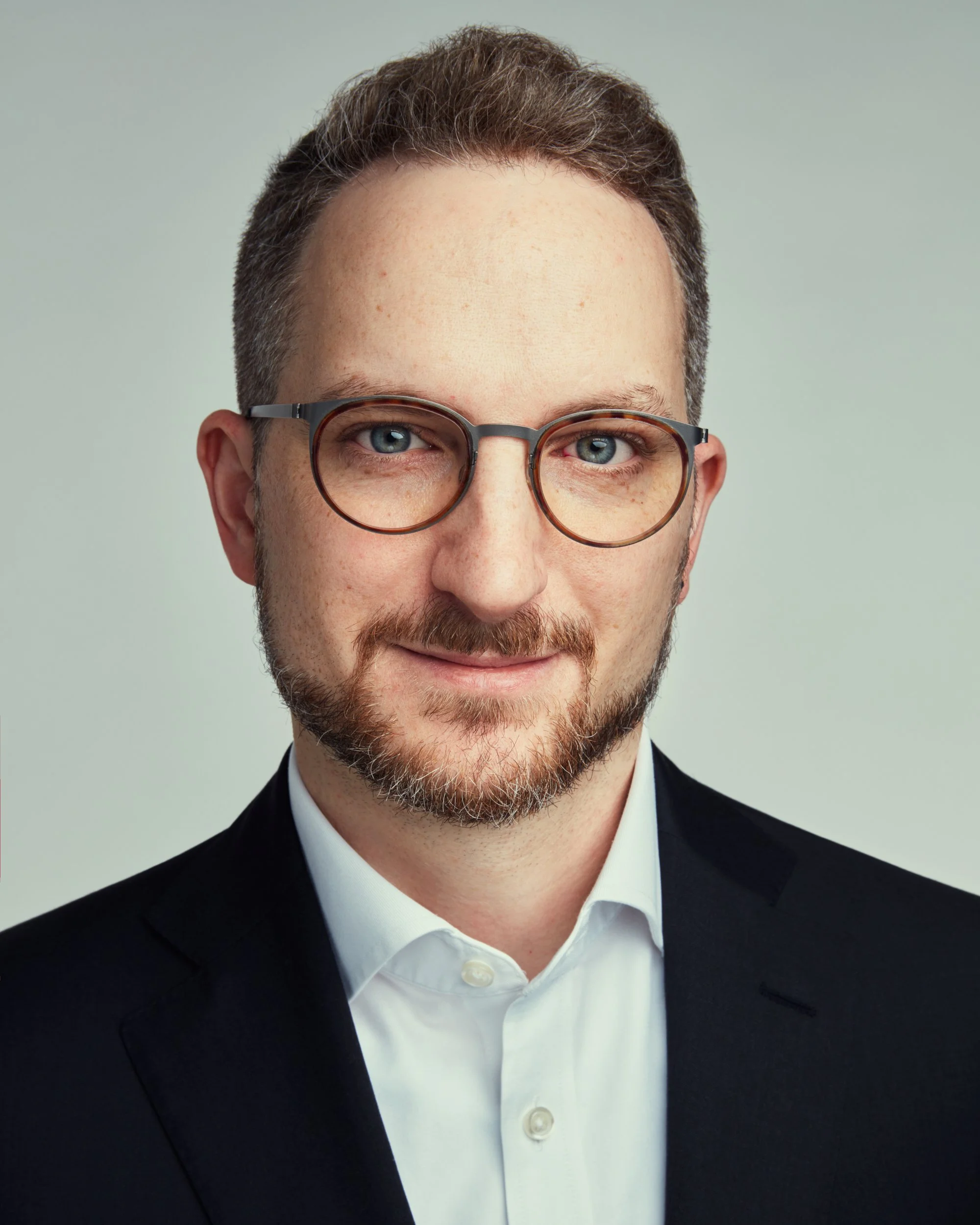 Business headshot of a professional man in a suit and glasses, Luke Nugent Portraits London