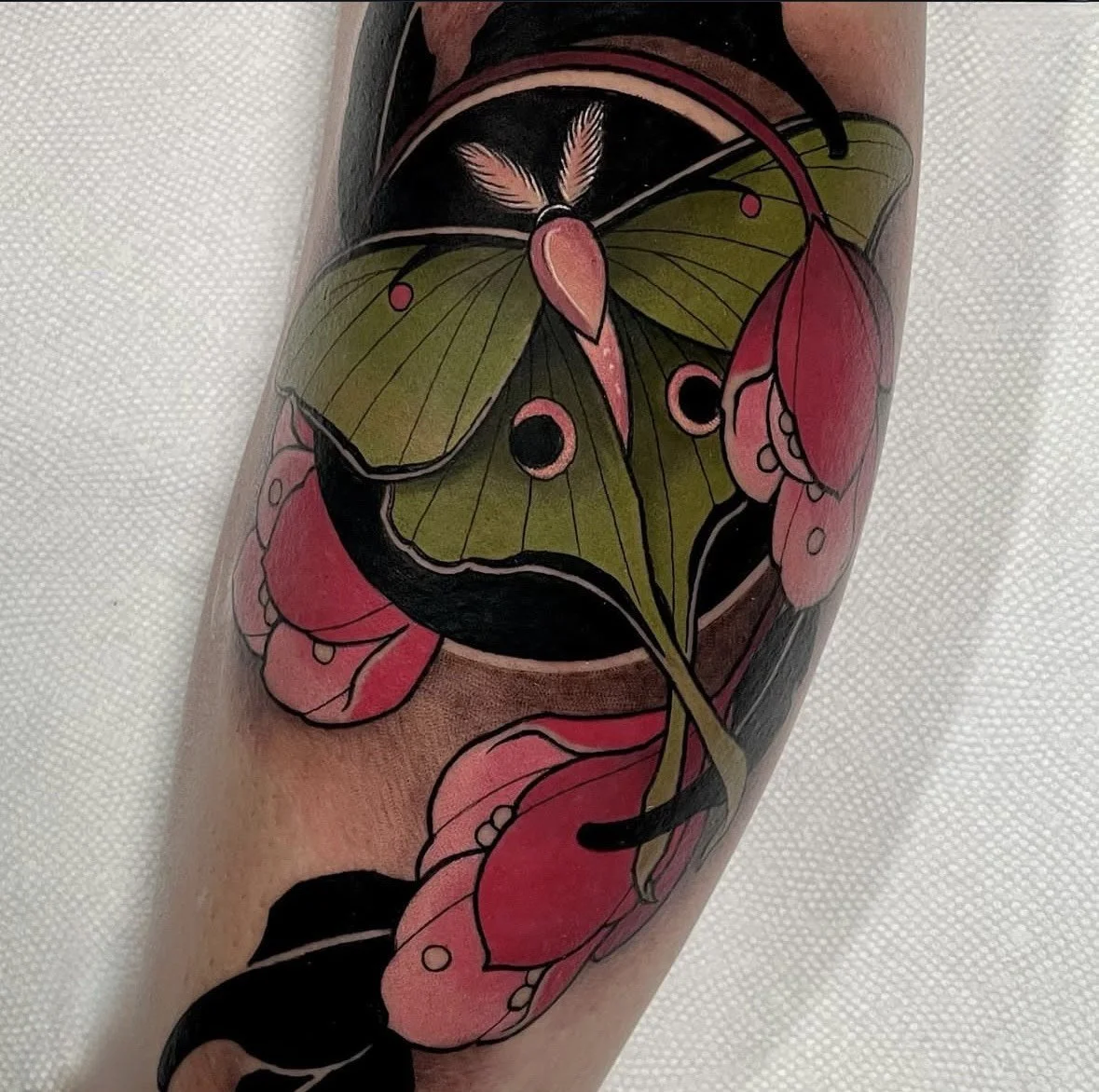 Tattoo of a green moth surrounded by pink hibiscus flowers