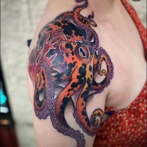 Colorful tattoo of an octopus with purple, orange, and black details on a person's upper arm.