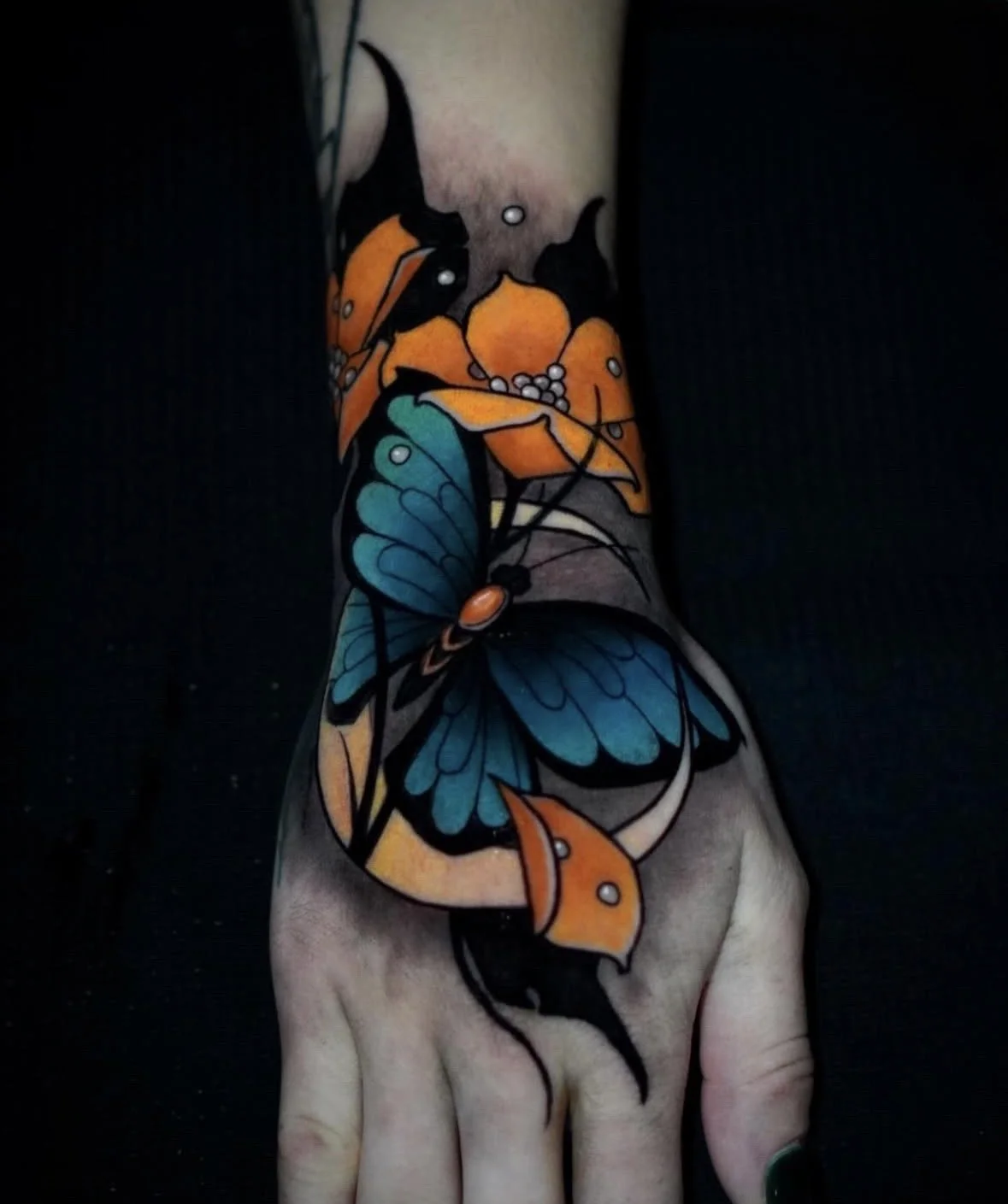 Colorful tattoo of orange and blue butterflies and leaves on a person's arm.