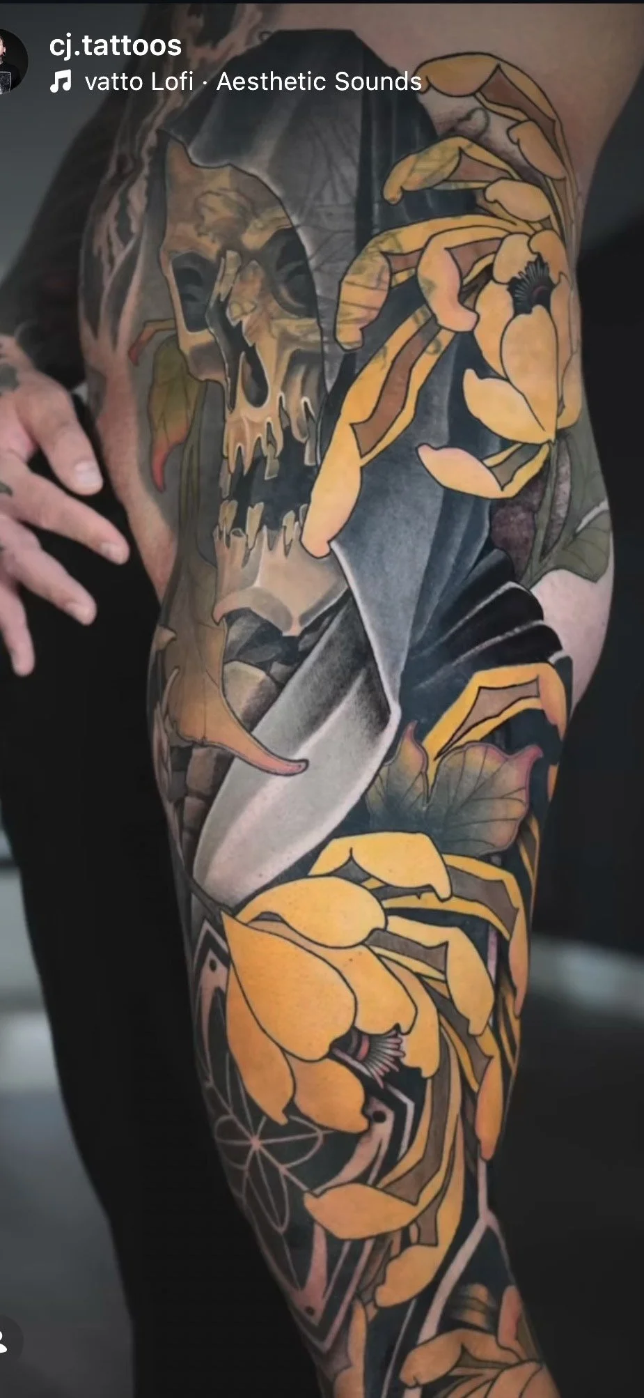 Close-up of a tattoo sleeve featuring a skull with a floral design in shades of yellow, orange, black, and gray on a person's arm.