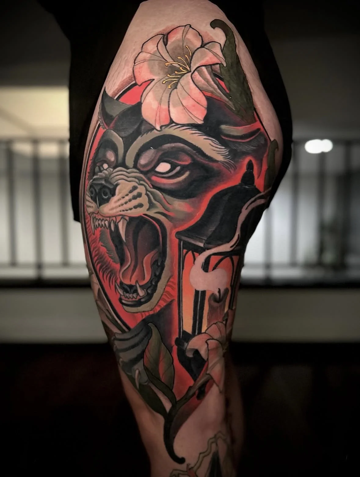 Tattoo of a snarling bear or dog face with flowers, leaves, and a lantern on the arm.