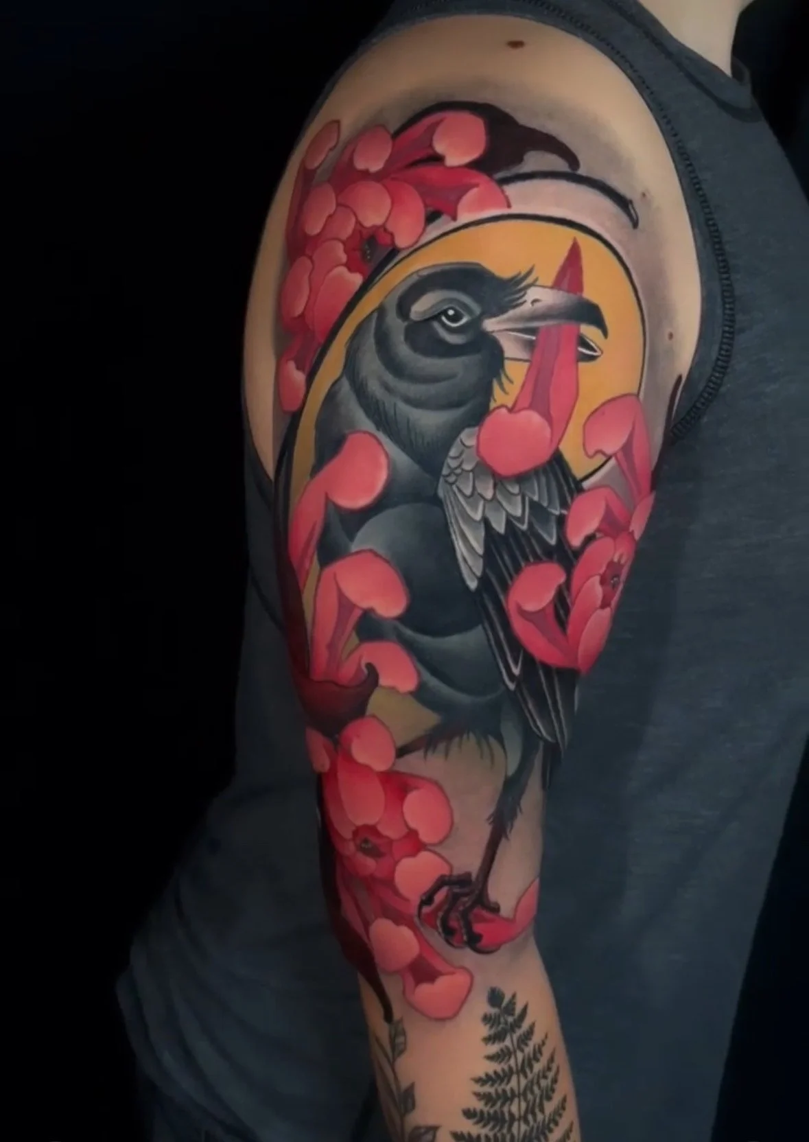 Tattoo of a black and gray bird surrounded by pink cherry blossom flowers on a person's upper arm.