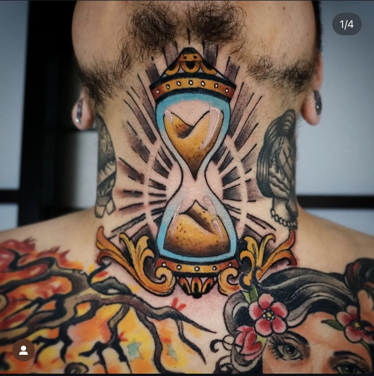 Colorful tattoo of an hourglass with a cake inside, featuring a crown on top, surrounded by radiating lines on a person's neck and chest with additional tattoos of flowers, a bird, and other designs.