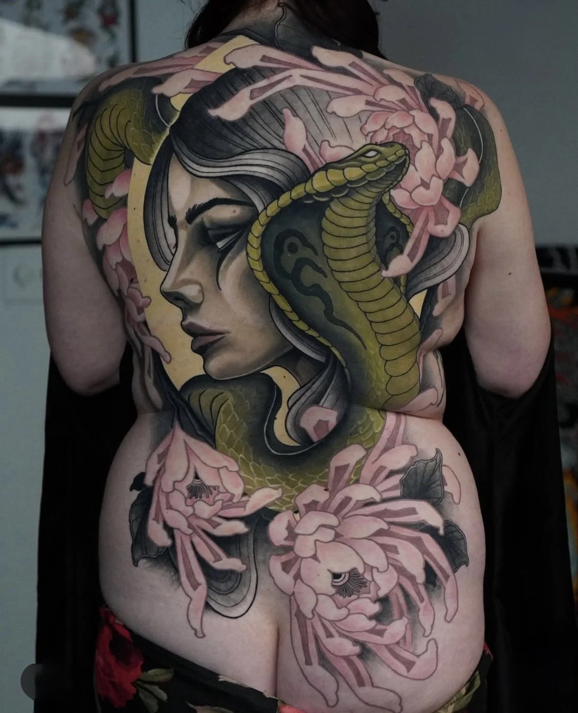 Tattoo of a woman's face, a snake, and pink flowers on person's back.