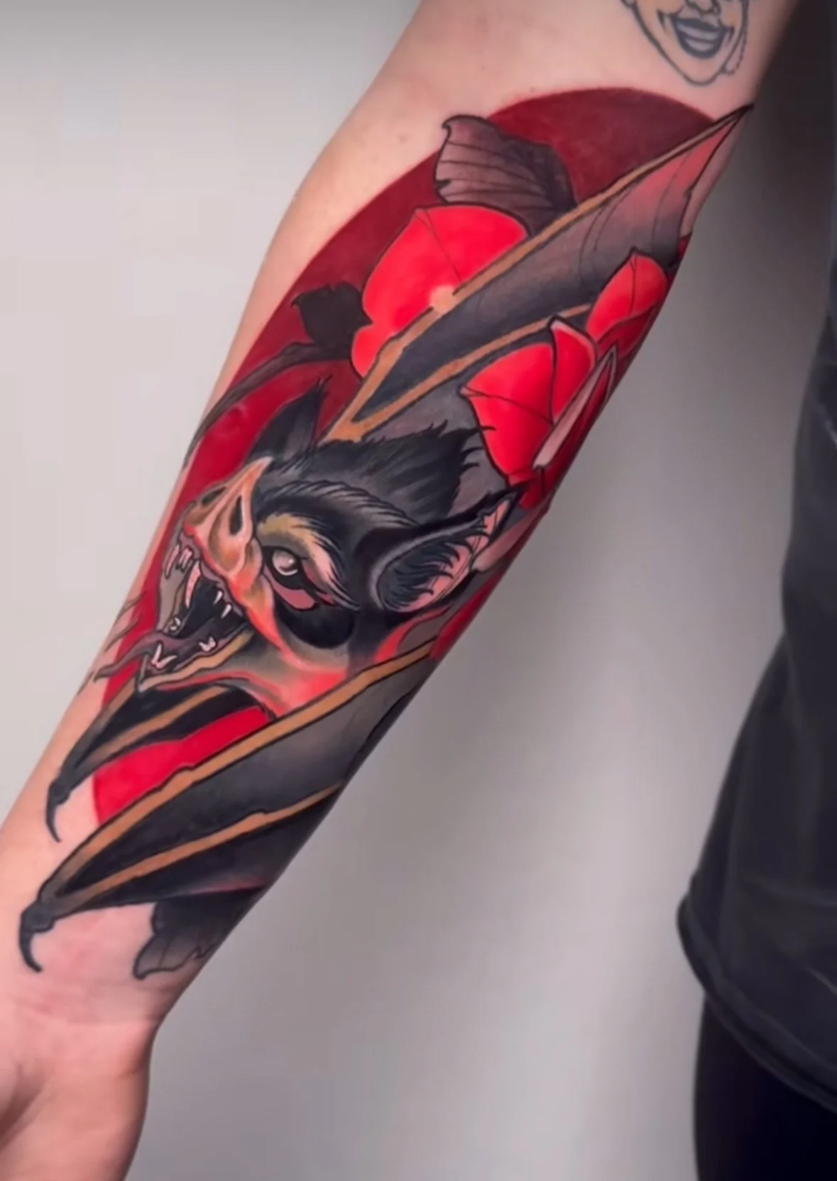 Tattoo of a wolf's head with red leaves and a red background on an arm.