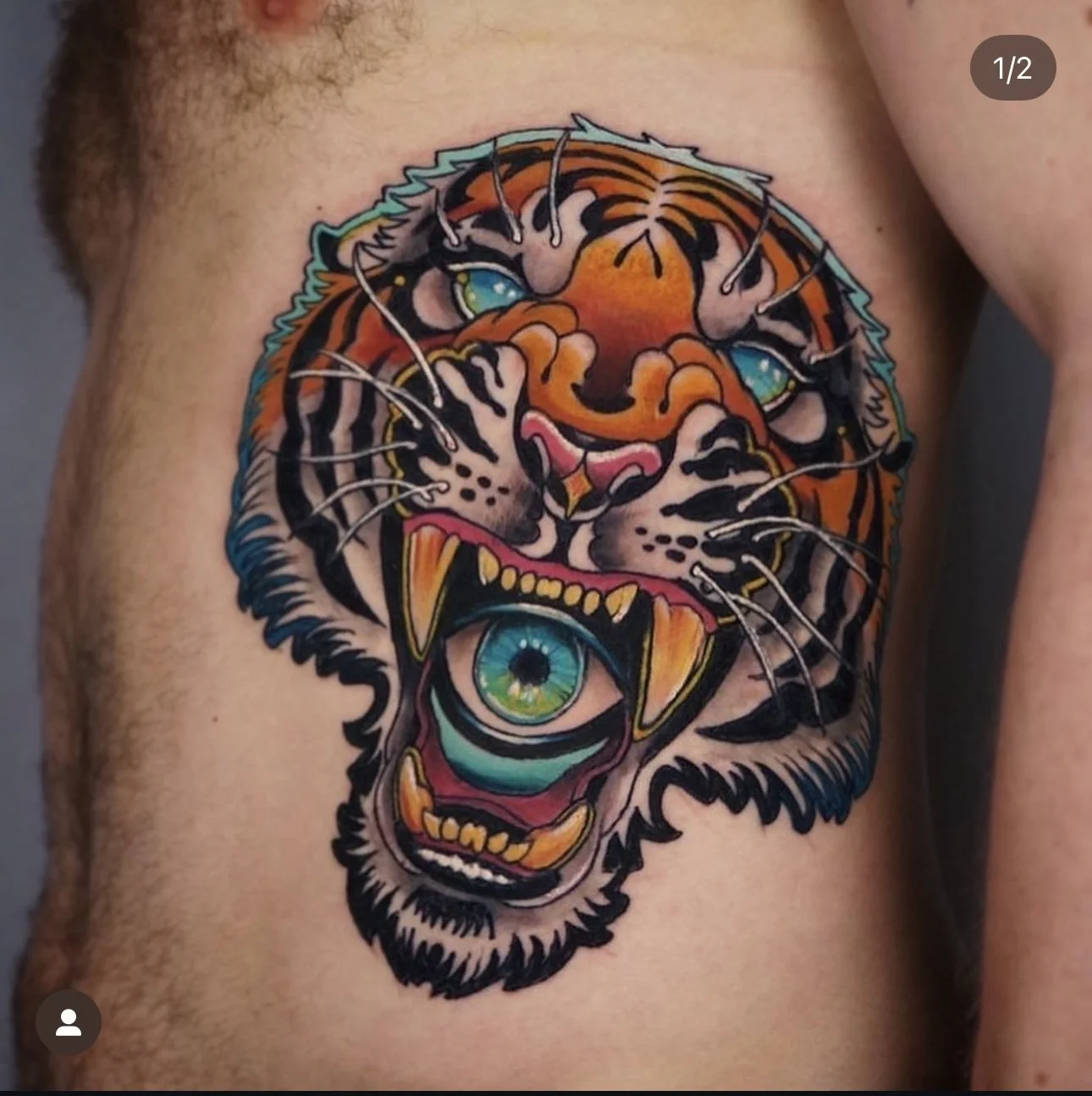 Colorful tattoo of a tiger's face with an eye in its mouth on a person's chest.