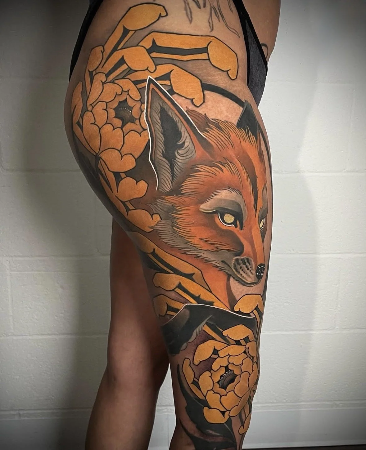 Tattoo of a fox surrounded by orange leaves on a person's thigh.