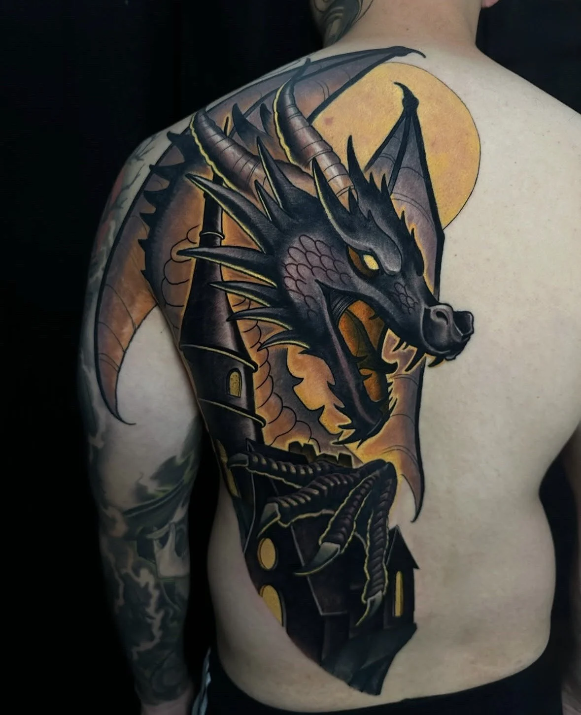 Tatted dragon with a castle, full moon, and dark sky on person's back.