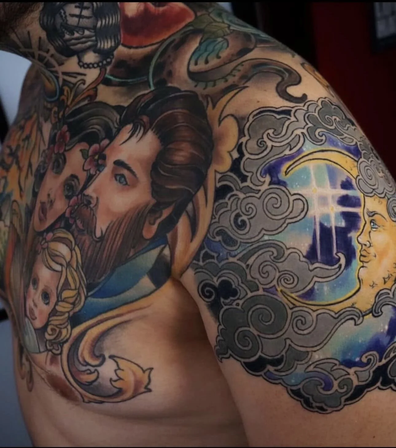 Tattoo of a woman with dark hair and a man with a beard, surrounded by clouds and a crescent moon with a face, on a person's shoulder and upper arm.