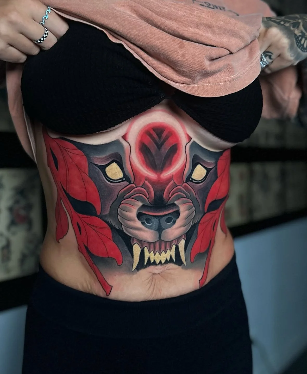 Tattoo of a stylized wolf or lion face with red, black, and yellow colors on a person's abdomen.