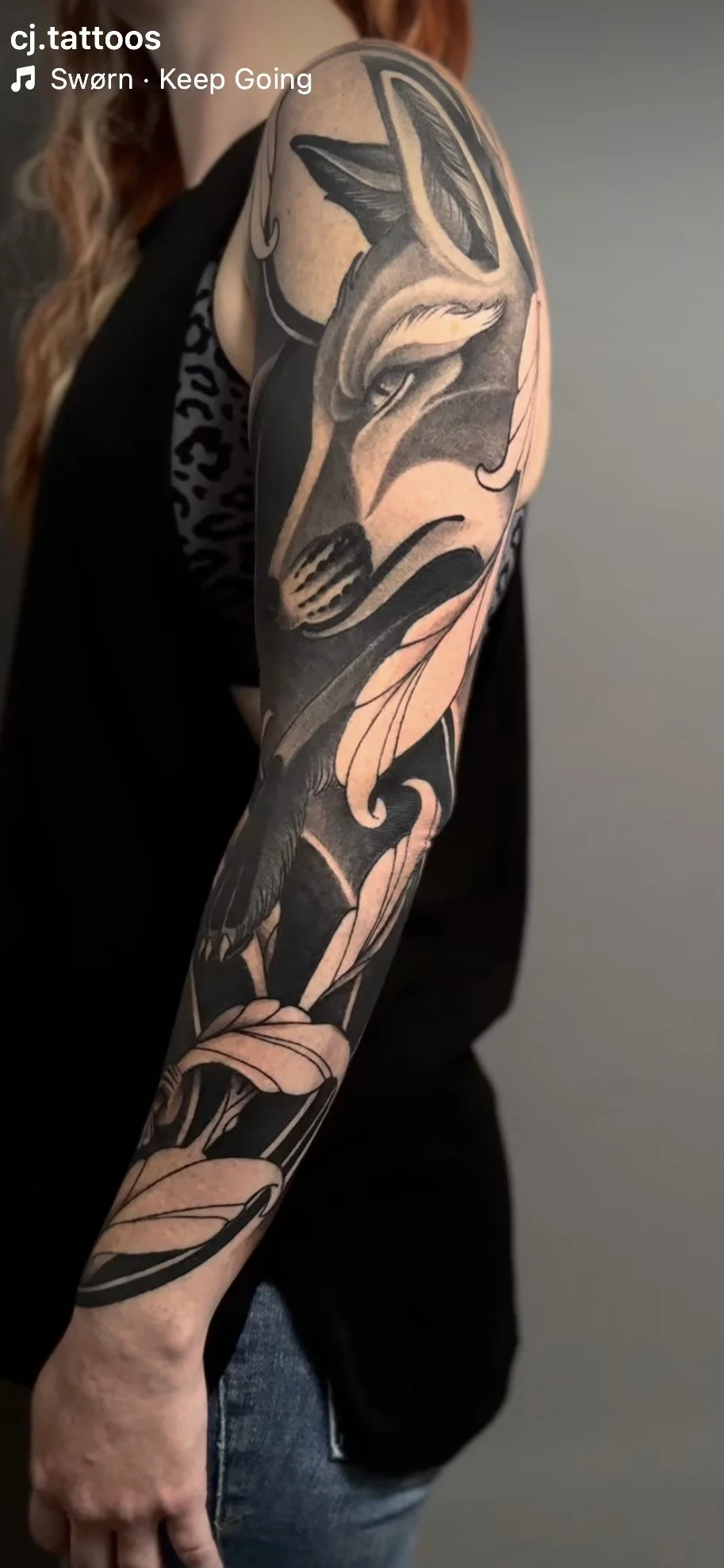 Close-up of a person's arm with a large, detailed black and grey tattoo featuring a wolf's head and floral elements.