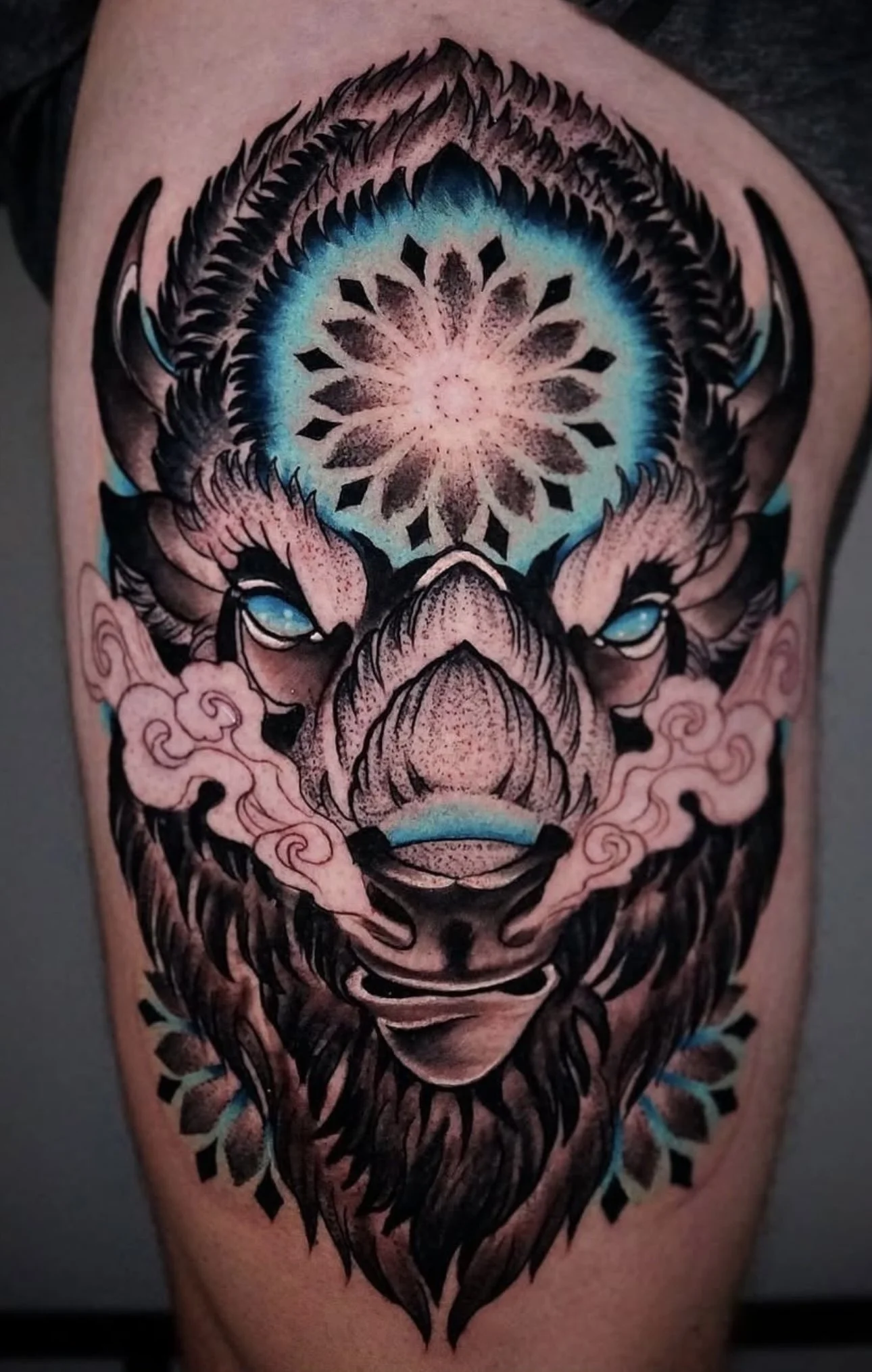 Tattoo of a stylized wolf with blue eyes, surrounded by pink smoke and snowflake patterns on the forehead.