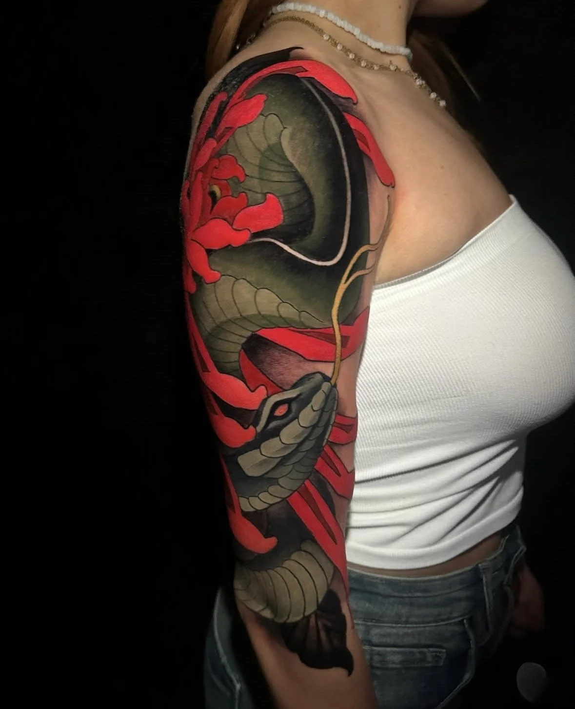 Tattoo of a snake intertwined with a cherry blossom branch on a woman's upper arm and shoulder.