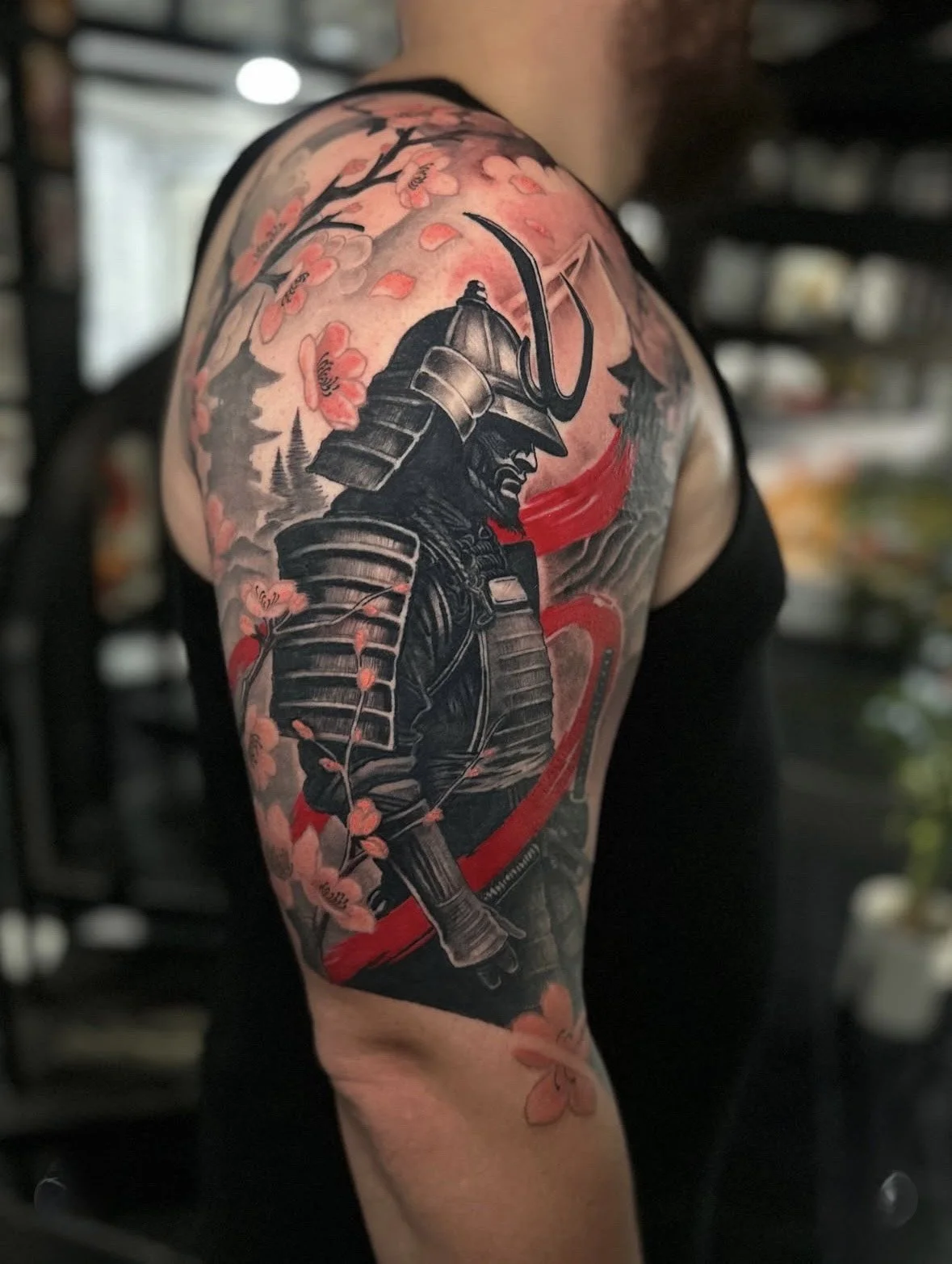 Tattoo of a samurai in black armor with cherry blossoms in pink around him.