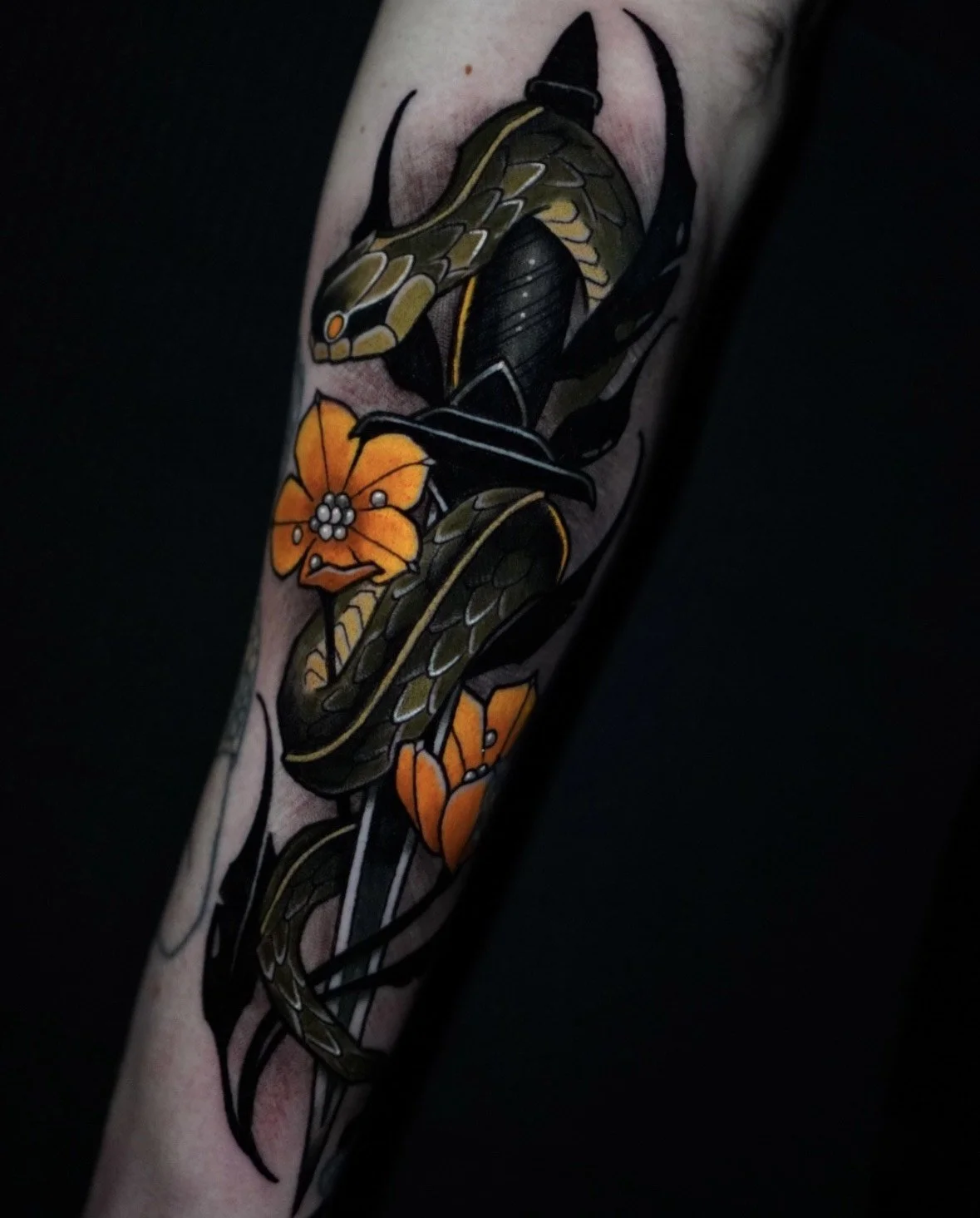 Tattoo of a snake, butterfly, and orange flowers on a person's arm.