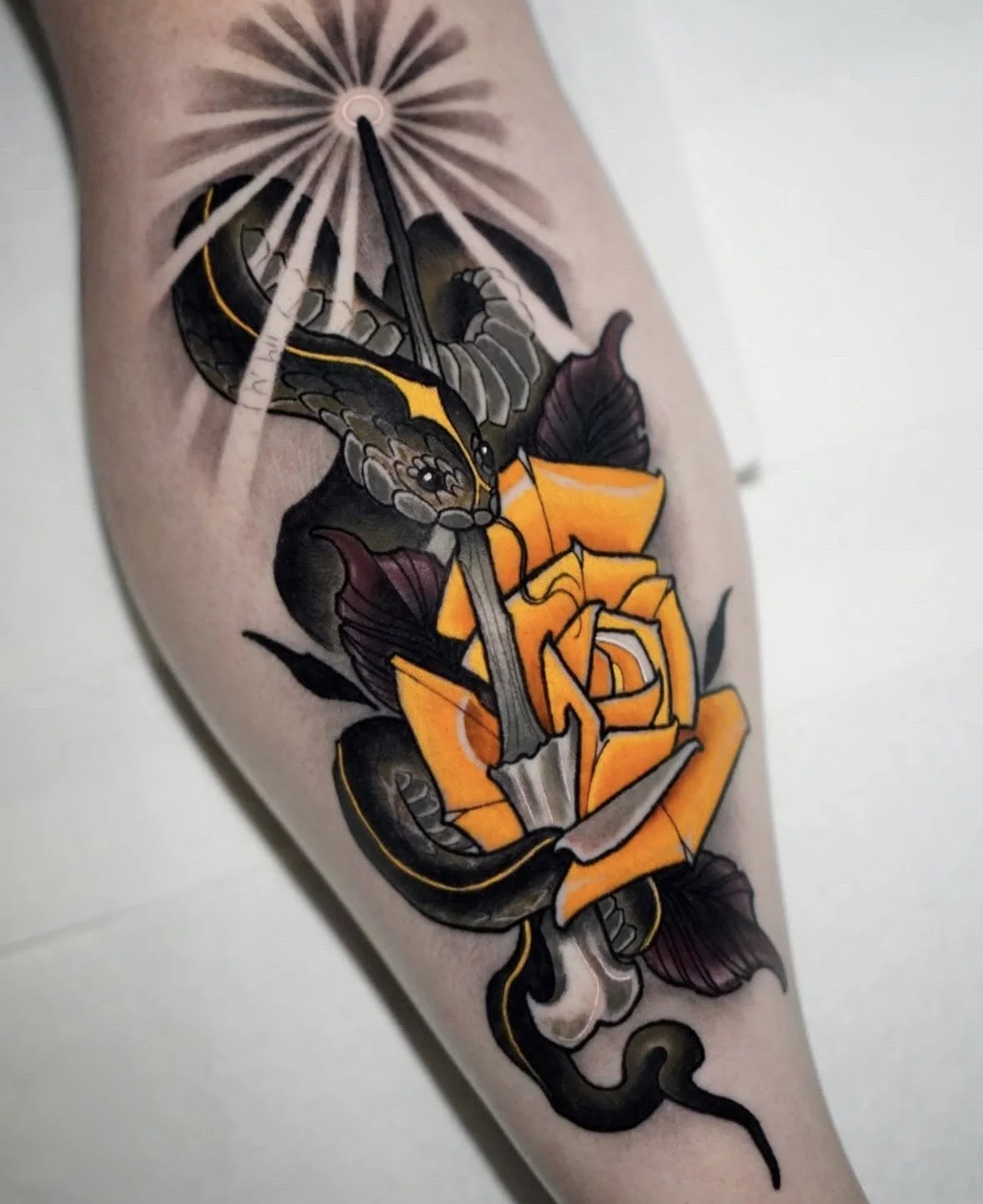 Tattoo of a snake wrapped around a yellow flower, with a butterfly at the top and a starburst pattern above.