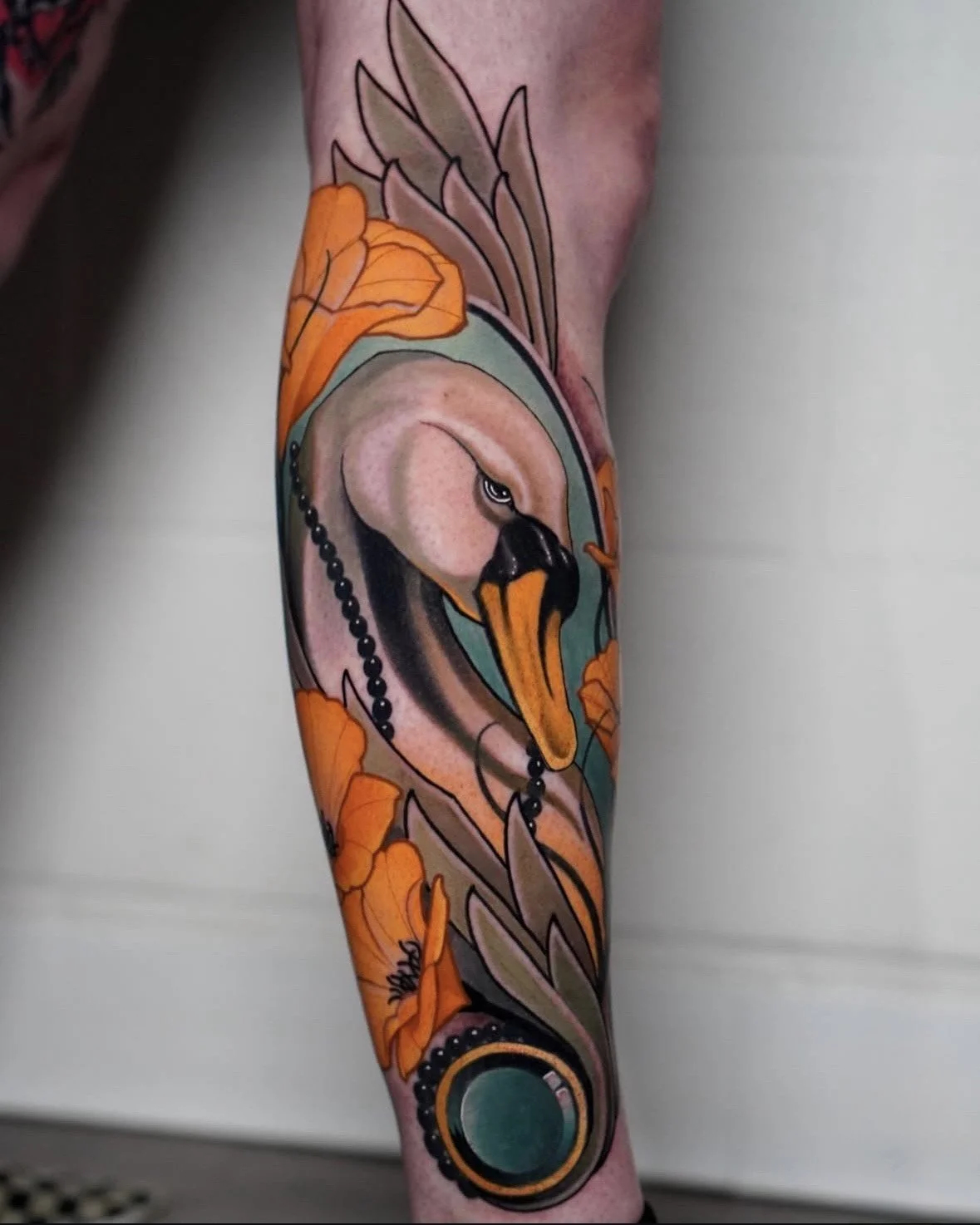 Tattoo of a swan with orange flowers and green accents on a person's arm.