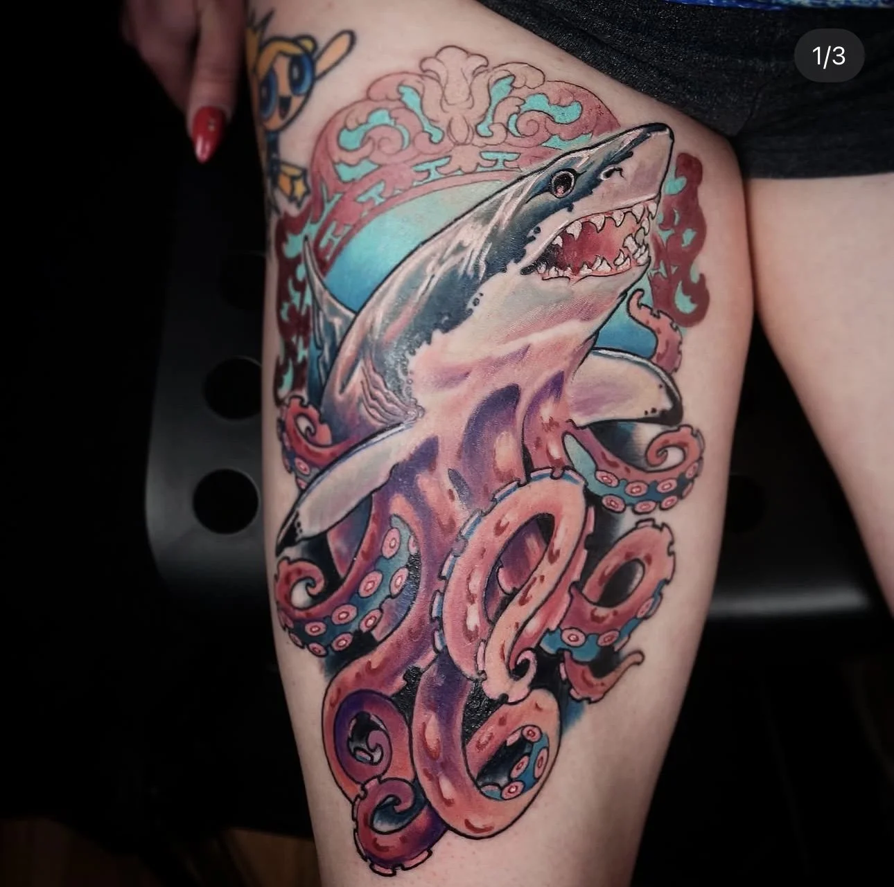 Colorful tattoo of a shark and octopus on a person's thigh, with waves and water background.
