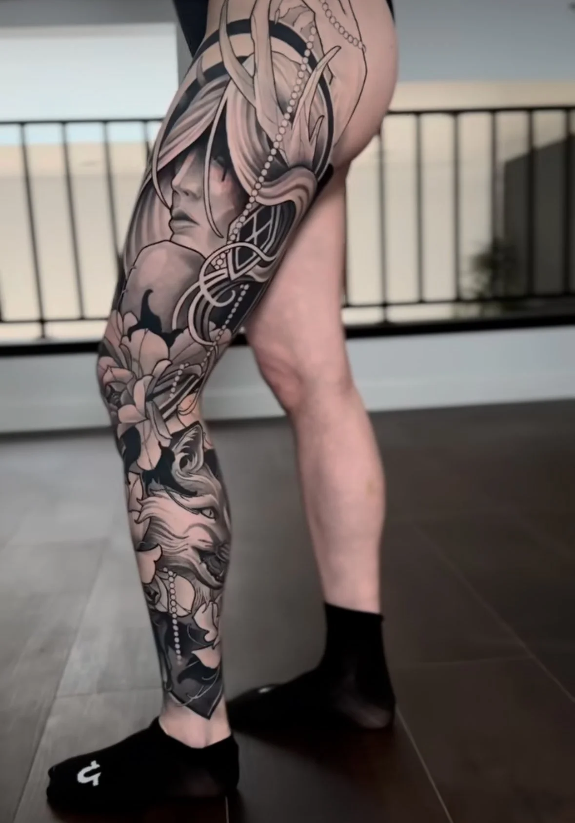 A person's leg with a detailed black and gray tattoo featuring a woman's face, flowers, and abstract designs, while wearing black Nike socks.