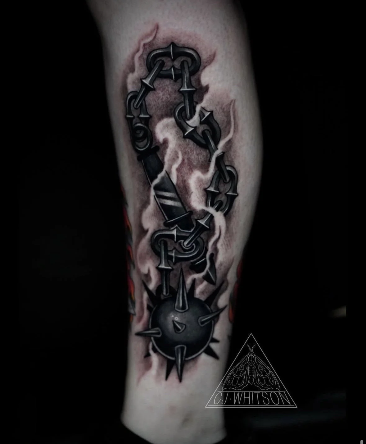 Tattoo of a chain linked to a spiked sphere, with the chain forming the shape of a person's face, on a person's arm.