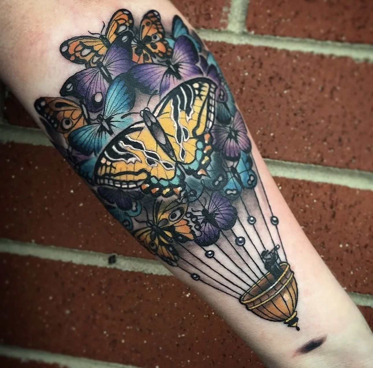 Colorful tattoo of butterflies flying out of a hot air balloon on a person's arm