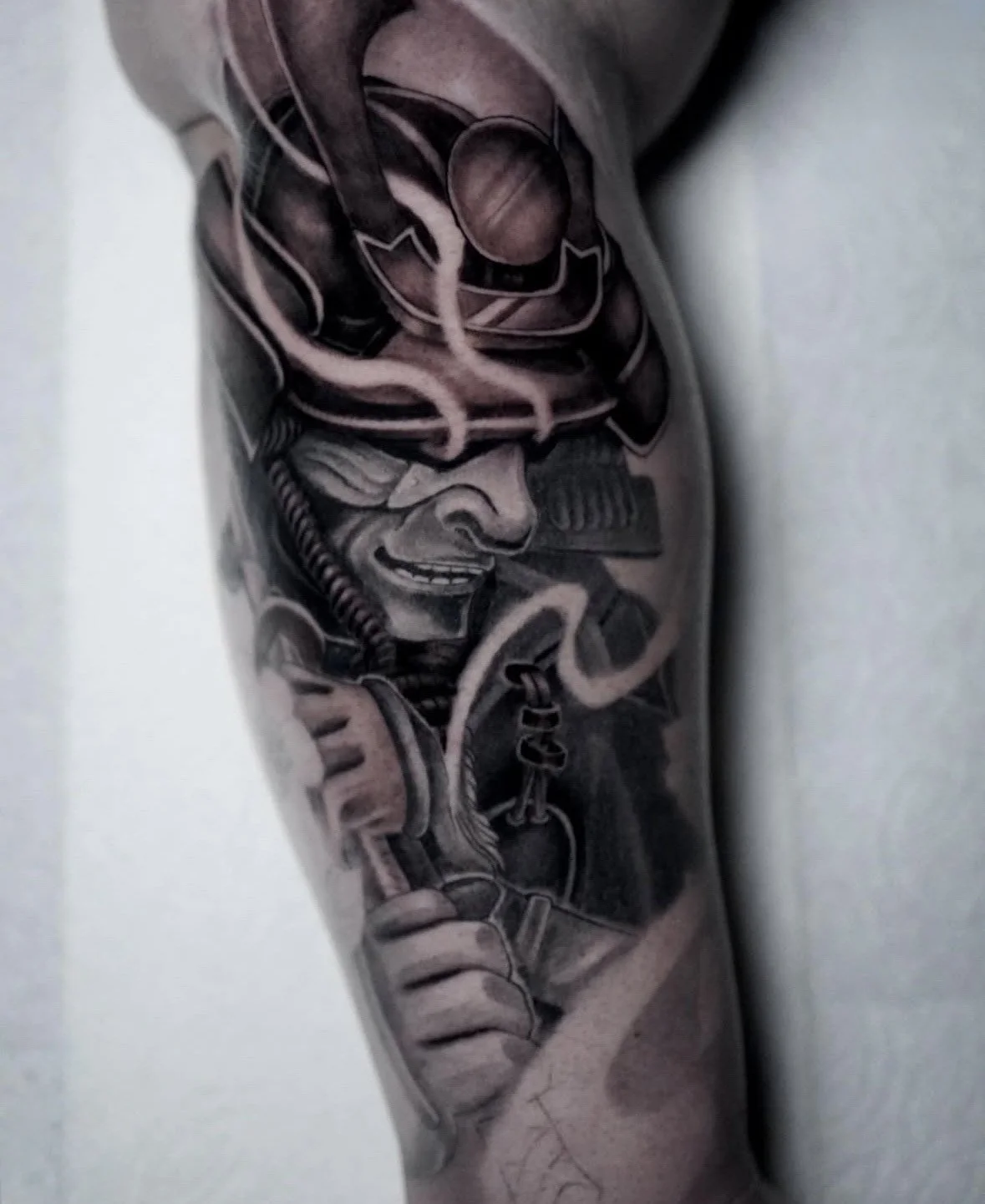 Black and gray tattoo of a smiling man wearing a helmet and goggles, holding a hose, with a confident expression.