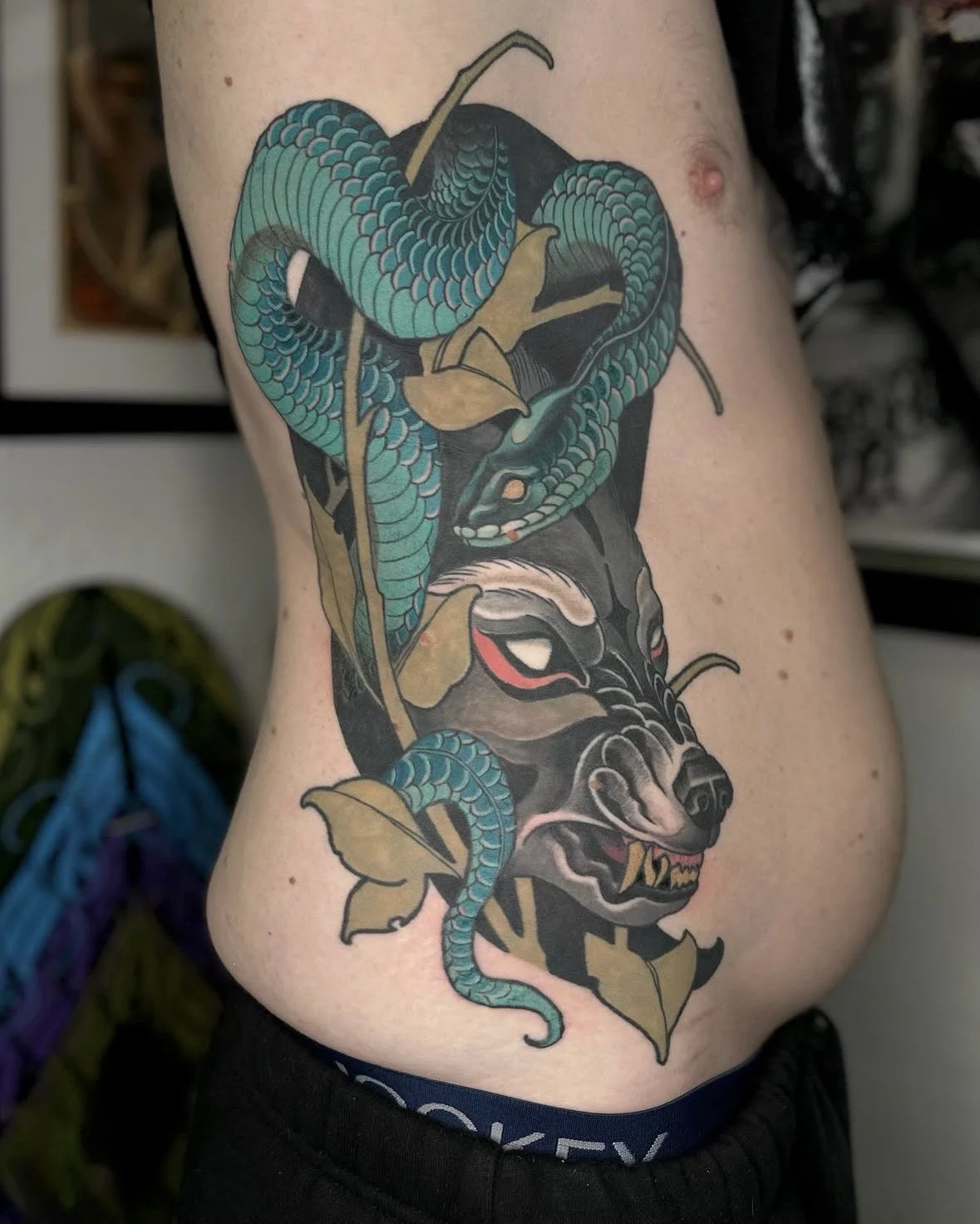 Tattoo of a snake intertwined with a tiger's face, with leaves around.