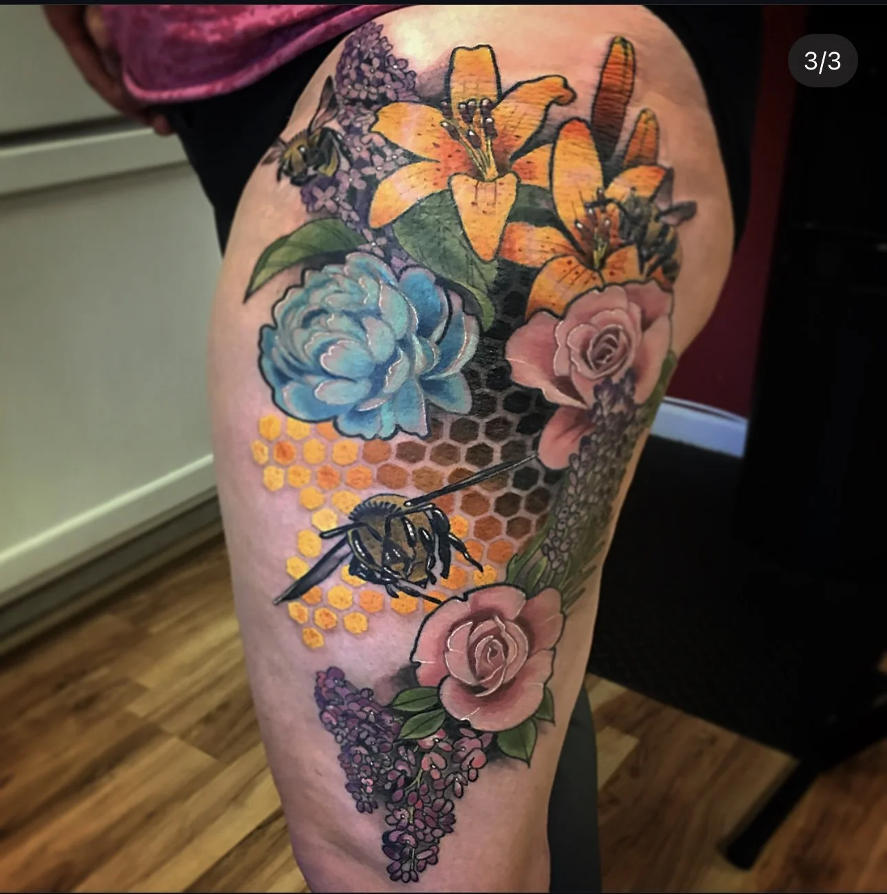 Colorful tattoo of flowers, bees, honeycomb pattern on a person's thigh.